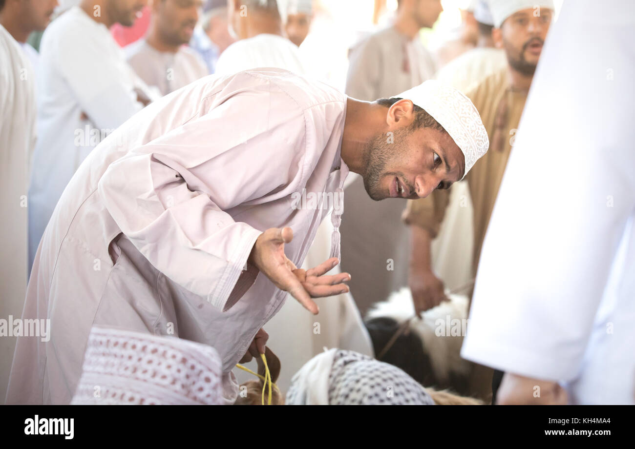 Omani man trying to sell a goat during a goat auction. Nizwa market, Oman. Stock Photo