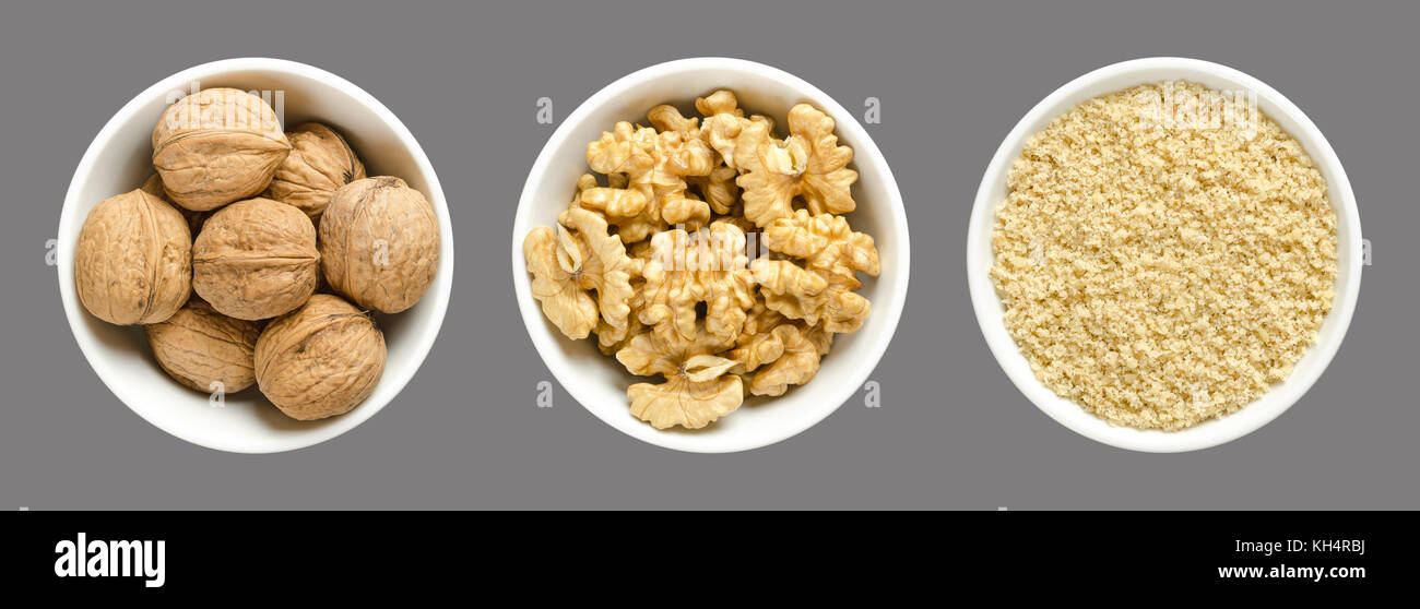 Whole, walnuts, kernel halves and ground walnuts in white bowls on gray background. Seeds of the common walnut tree Juglans regia. Stock Photo