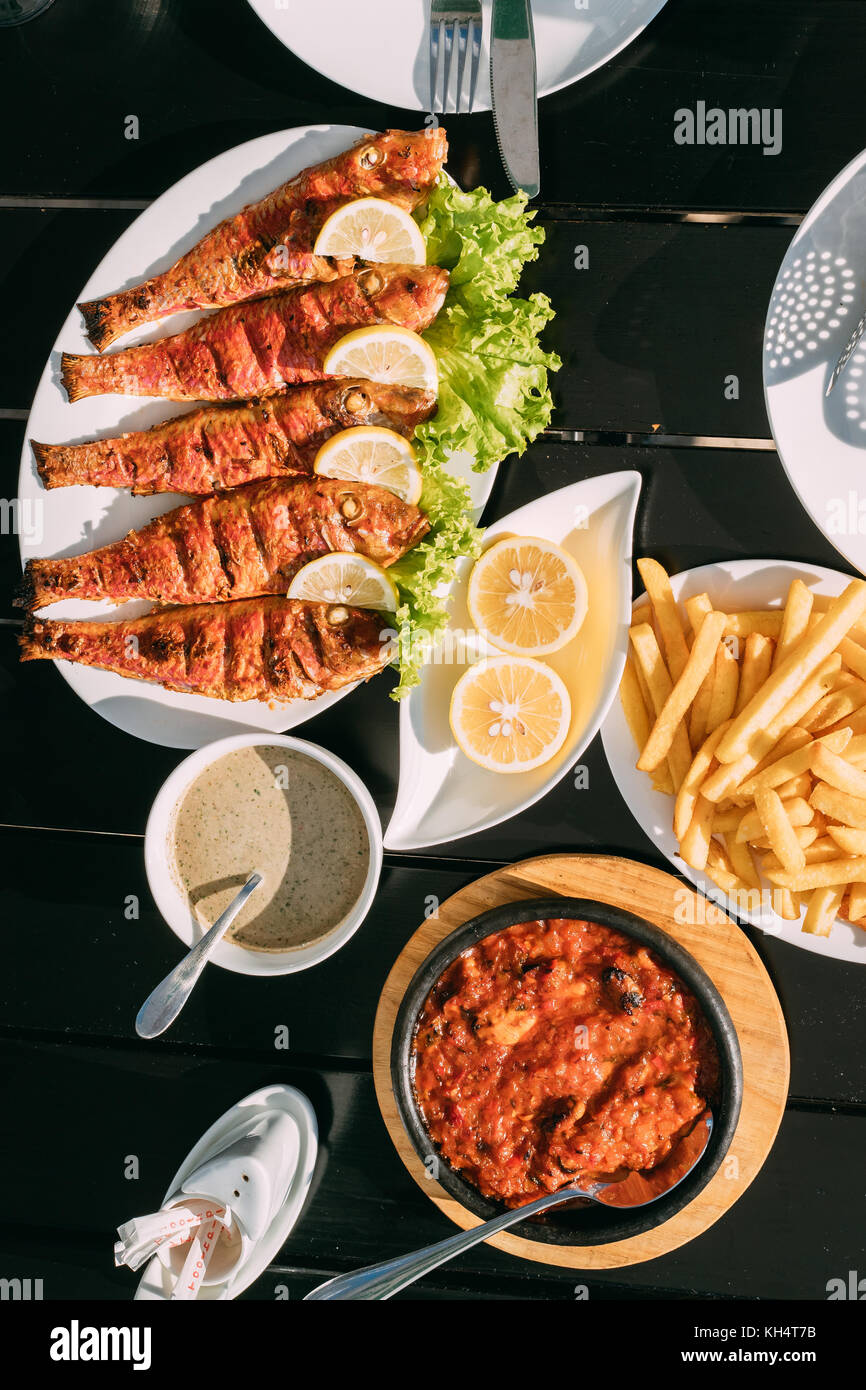 Batumi, Adjara, Georgia. Dishes Of Georgian National Cuisine: Fried Red Mullet Fish, Lemons, Satsivi Or Walnut Sauce, Stewed Mussels And French Fries. Stock Photo