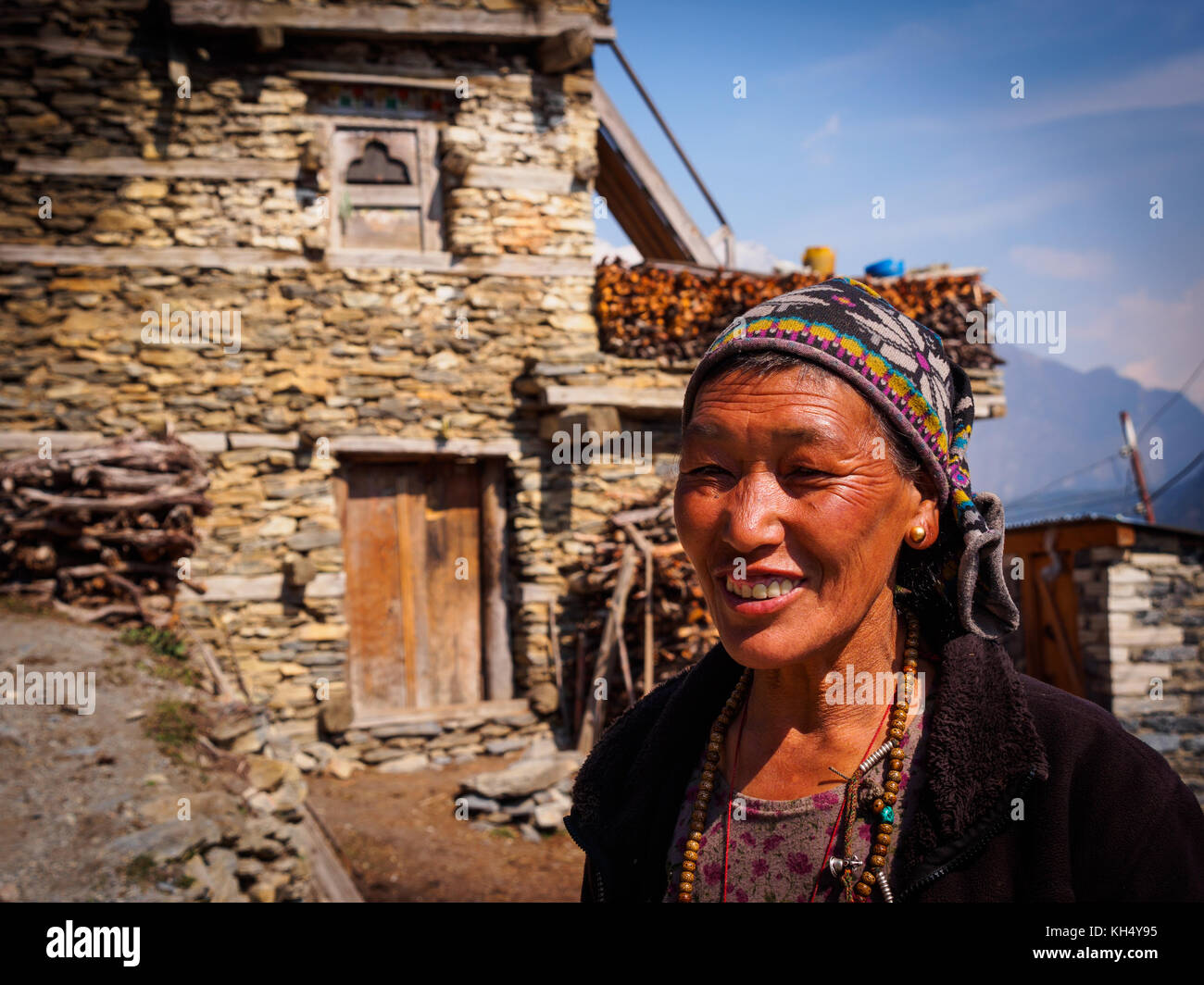 Weathered, smiling face of a Manangi woman in front of her traditional stone home in Upper Pisang village, Annapurna Circuit Trek, Nepal Stock Photo