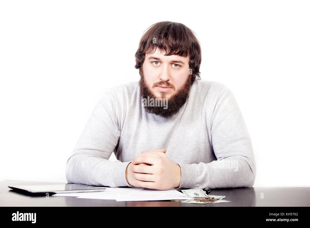 portrait of young businessman in beard, sitting in relaxed position at at office table with pleasant look. Confident male business person Stock Photo