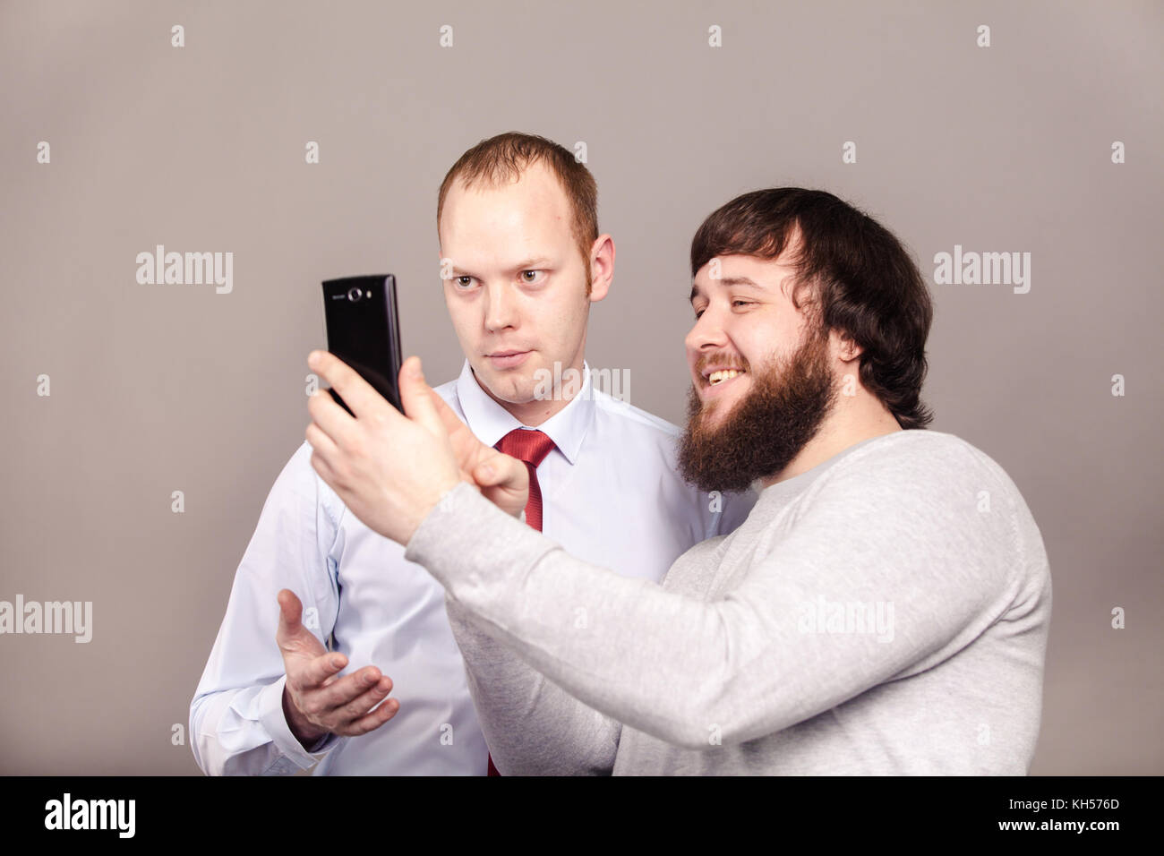 Two smiling colleagues taking the picture to them self, happy friends taking selfie with telephone camera on dark background Stock Photo