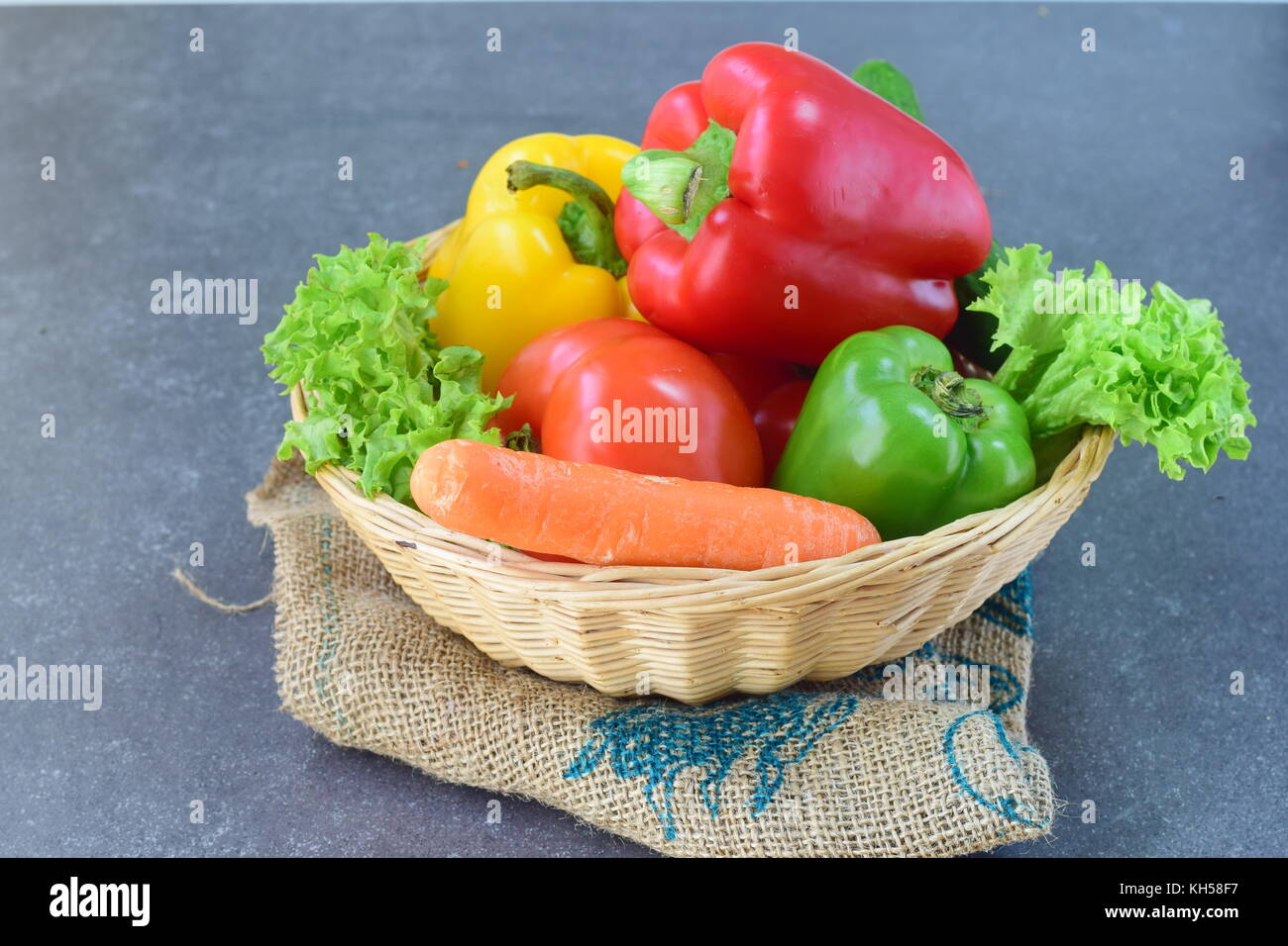 Fresh vegetables: paprika, tomato, onion,onion, carrot on a rustic textile cloth on a grey wooden background. Healthy eating concept Stock Photo