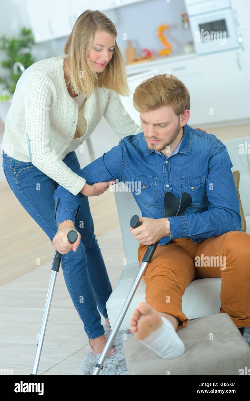 Lady helping man with crutches to stand up Stock Photo Alamy