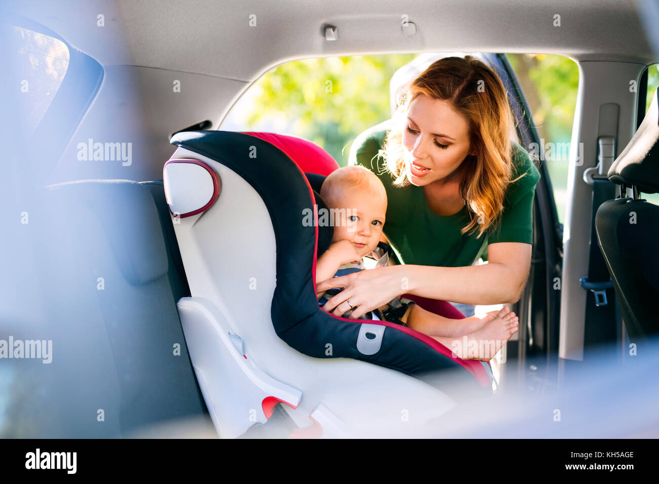 Young mother putting baby boy in the car seat. Stock Photo