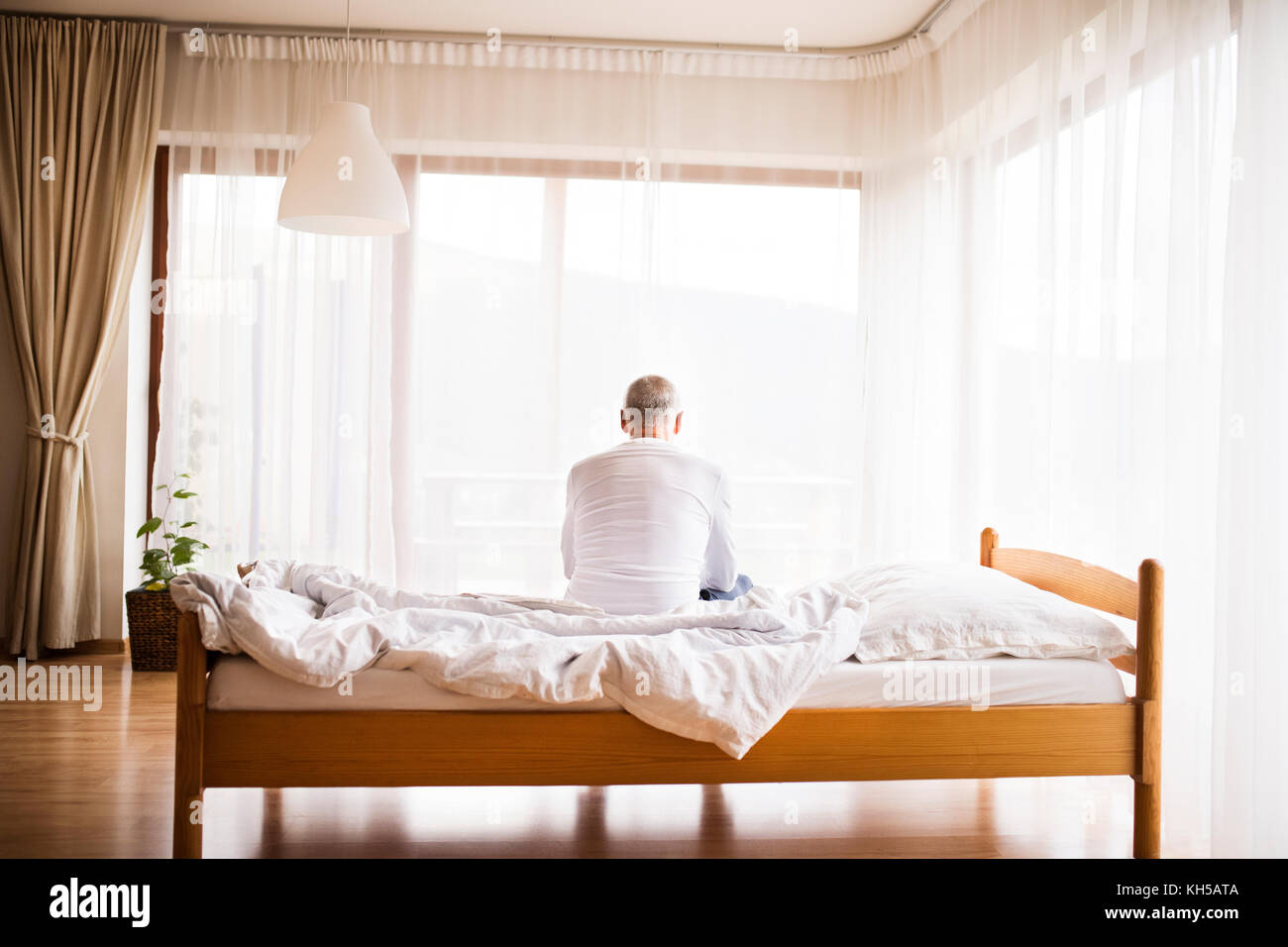 Senior man sitting on bed at home. Stock Photo