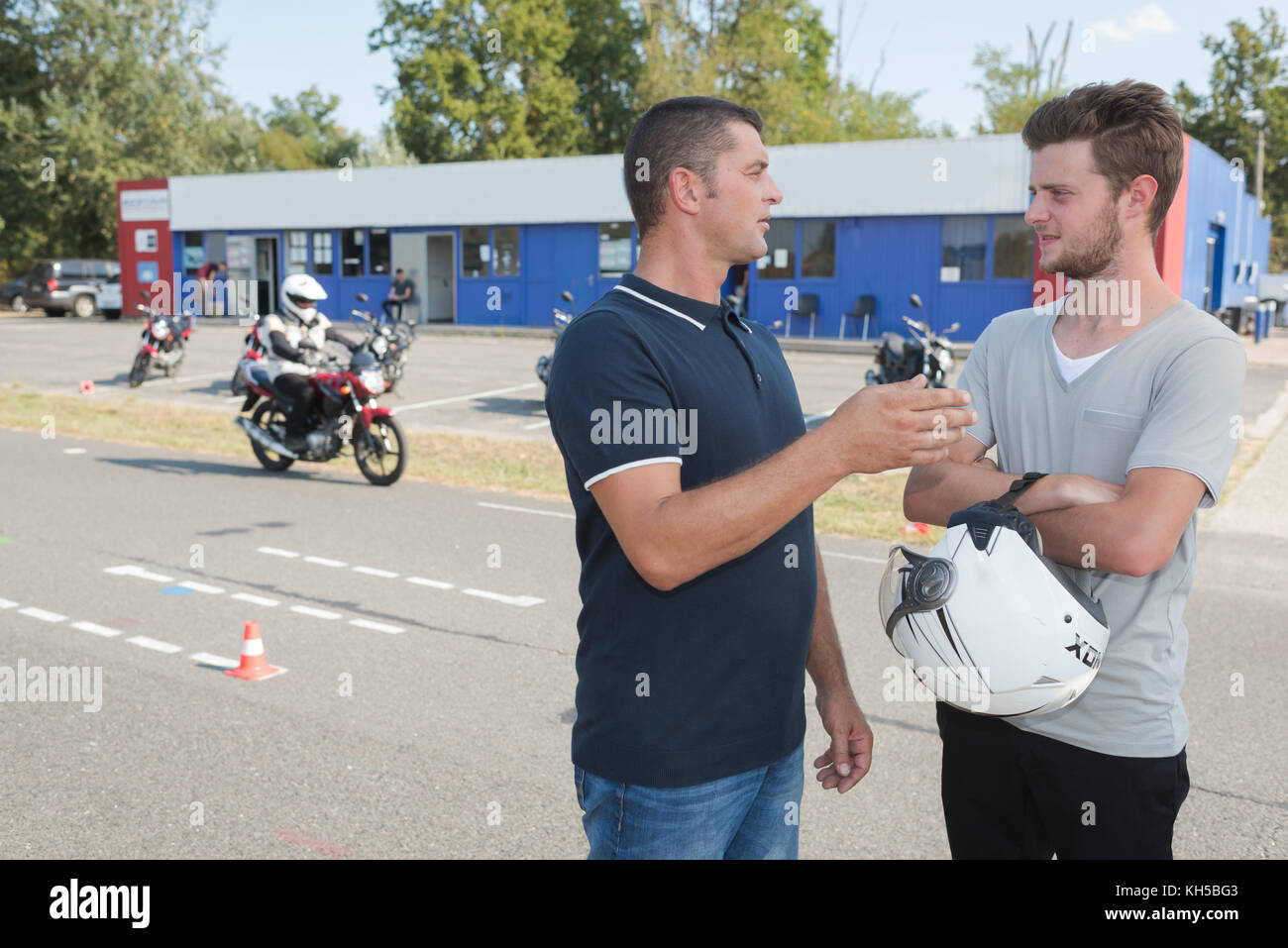 male driving instructor talks to motorcyclist before test Stock Photo
