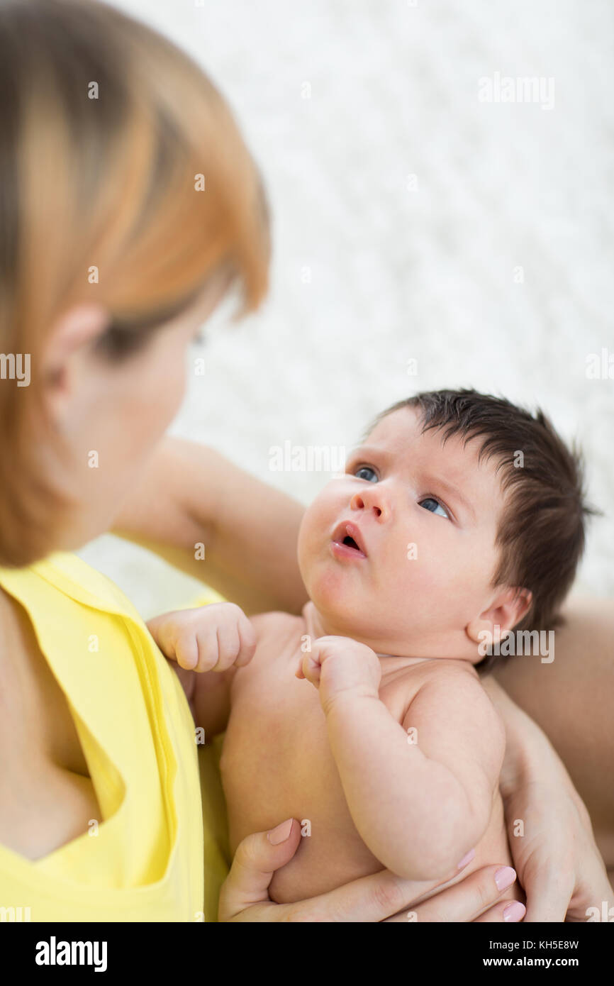 Side view of caring mother and her infant baby looking at each other, spending time together at home Stock Photo