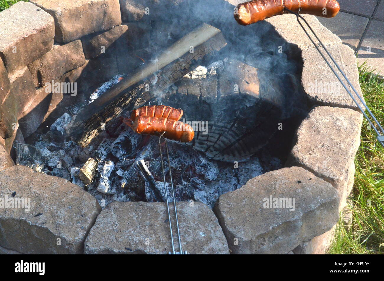 Two boys are grilling or barbecuing Polish sausages over an open fire pit in their backyard