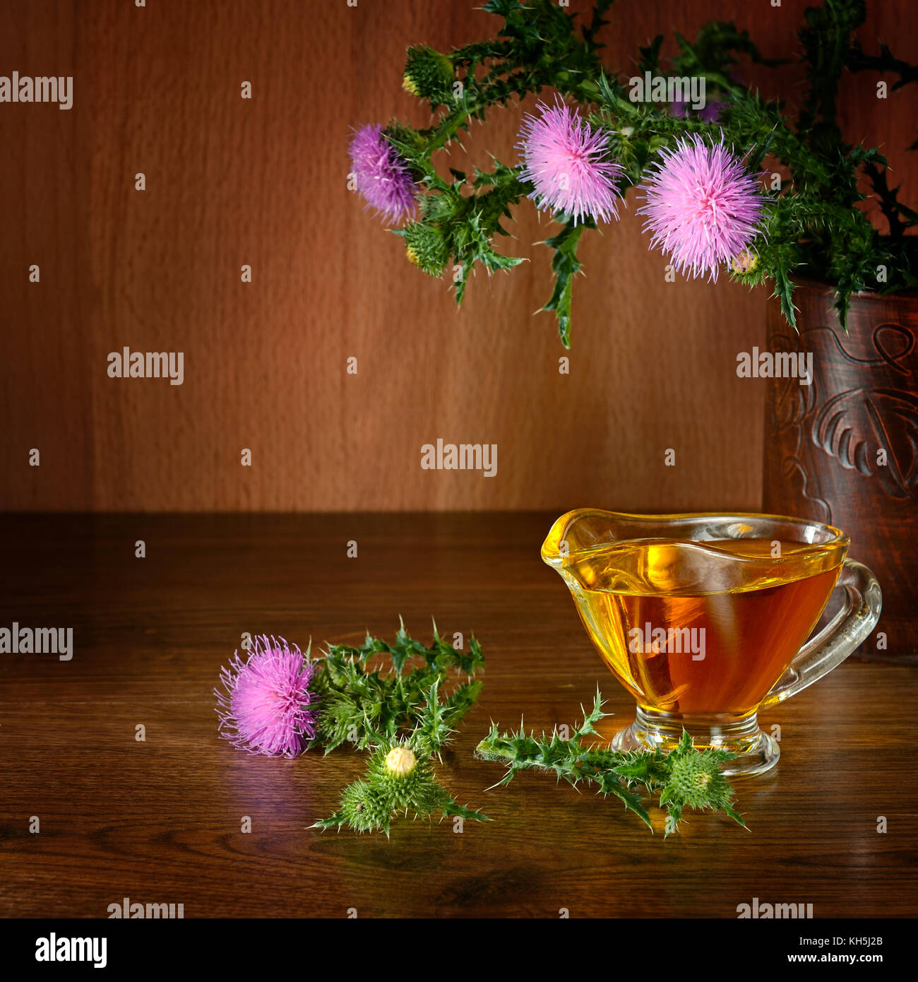 Flowering plant milk thistle and oil glass. Healing herb on wooden background. Free space for text. Stock Photo