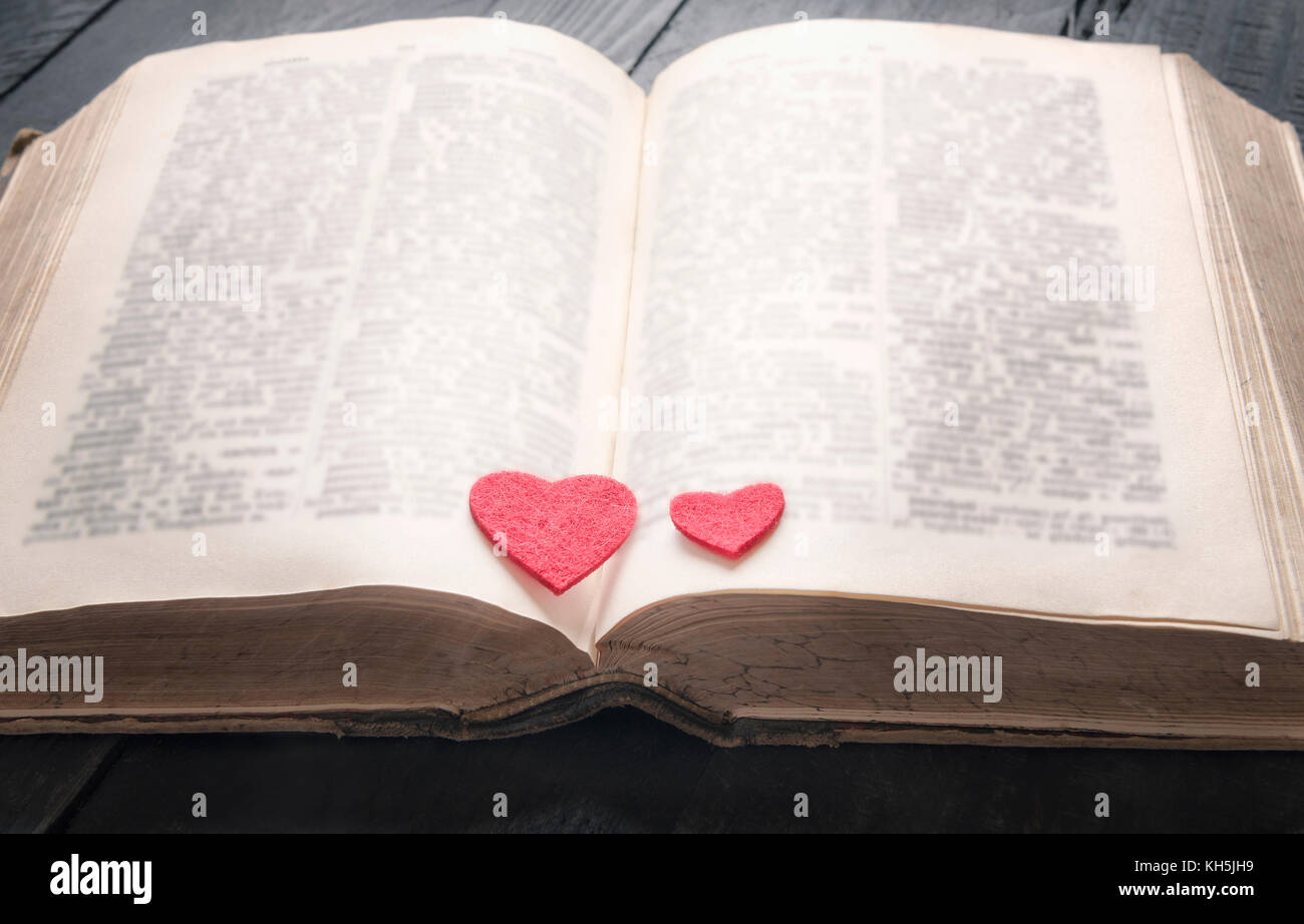 Two red hearts on the pages of an old open book, displayed on a vintage black table. A concept for the love of education,  a romantic novel or a love  Stock Photo