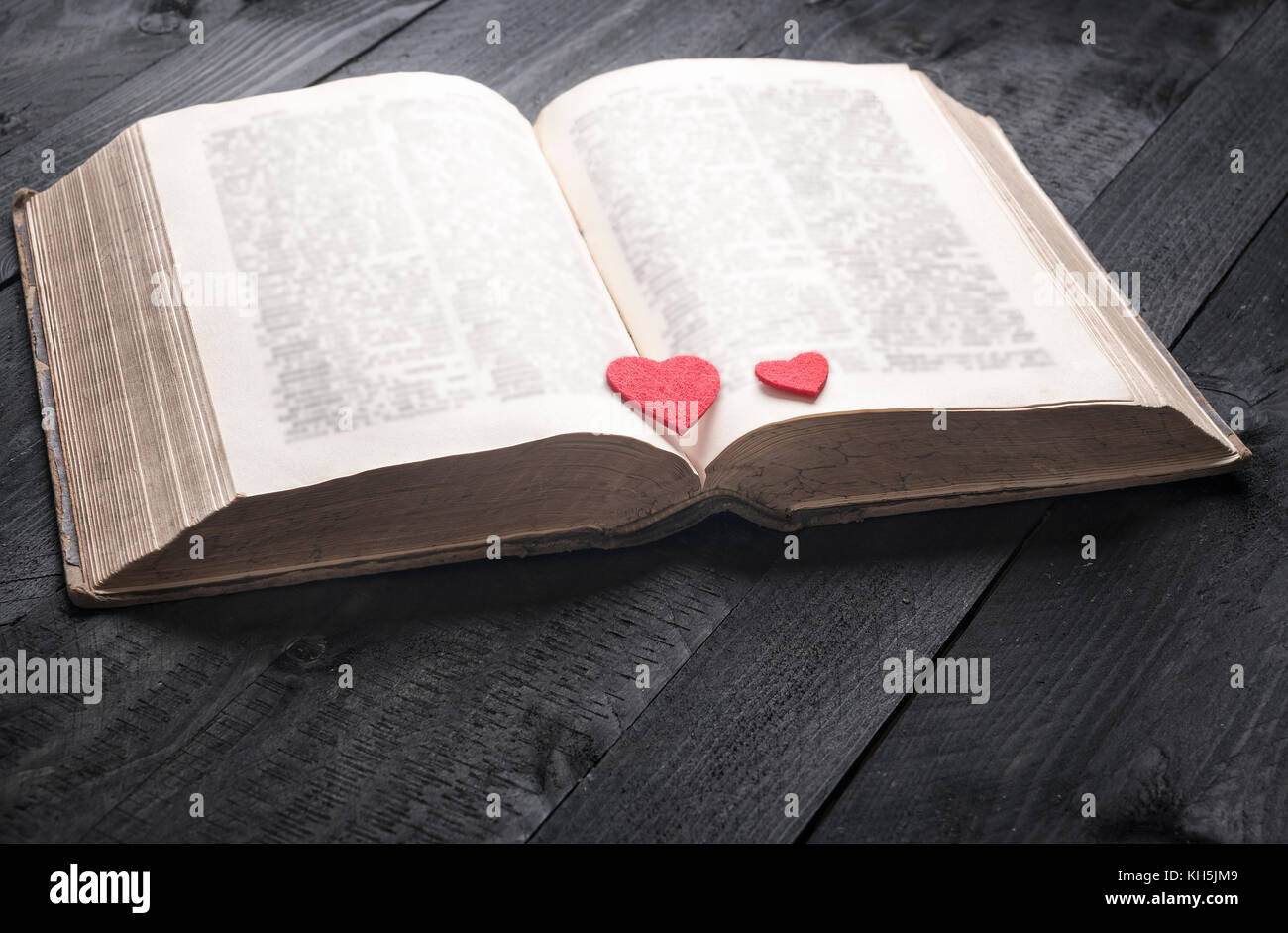 Schooling theme image with an antique open book and two red hearts on its pages, displayed on a vintage wooden table. A concept for reading,  studying Stock Photo