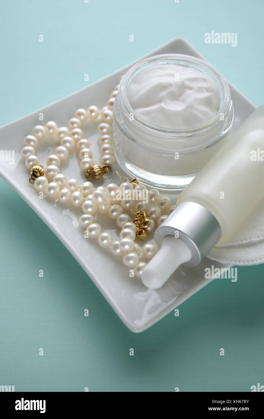 A jar of luxury beauty face cream and serum bottle with pearls on aqua