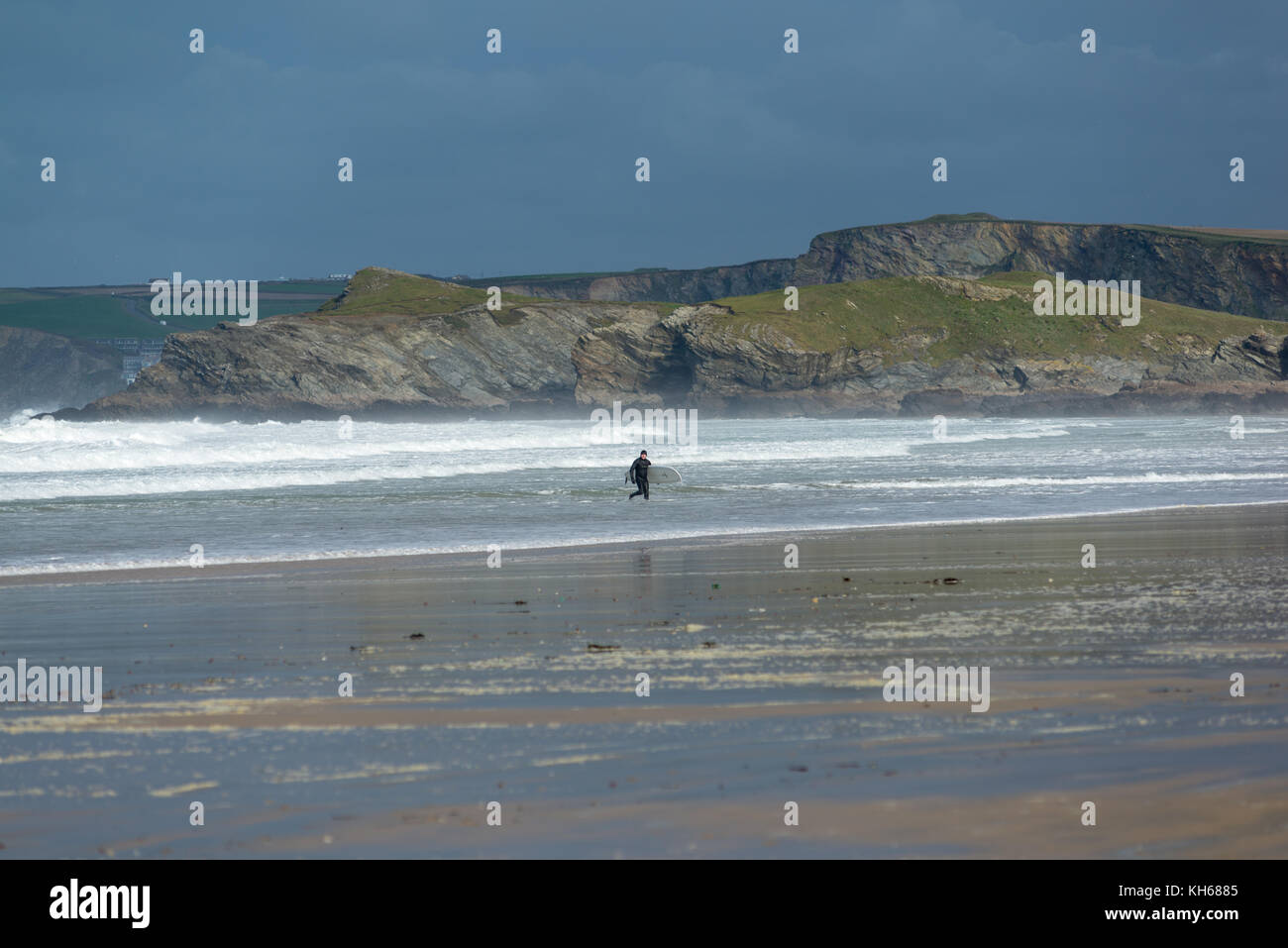 Surfer in a full wet suit on a sunny but windy autumn day on the beach at Newquay, Cornwall, UK. Stock Photo