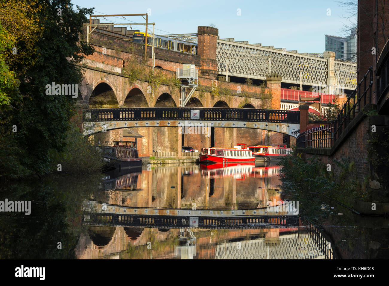 A footbridge, Victorian railway viaducts and canal boats reflected in the Bridgewater Canal at Castlefield, Manchester, England, UK. Stock Photo