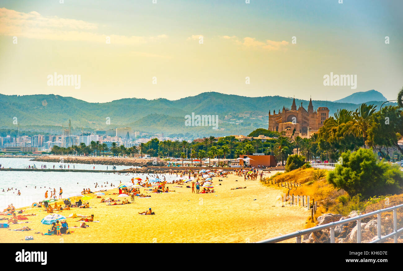 View of the beach of Palma de Mallorca with people lying on sand and the gorgeous cathedral building visible in background. Palma-de-Mallorca, Baleari Stock Photo
