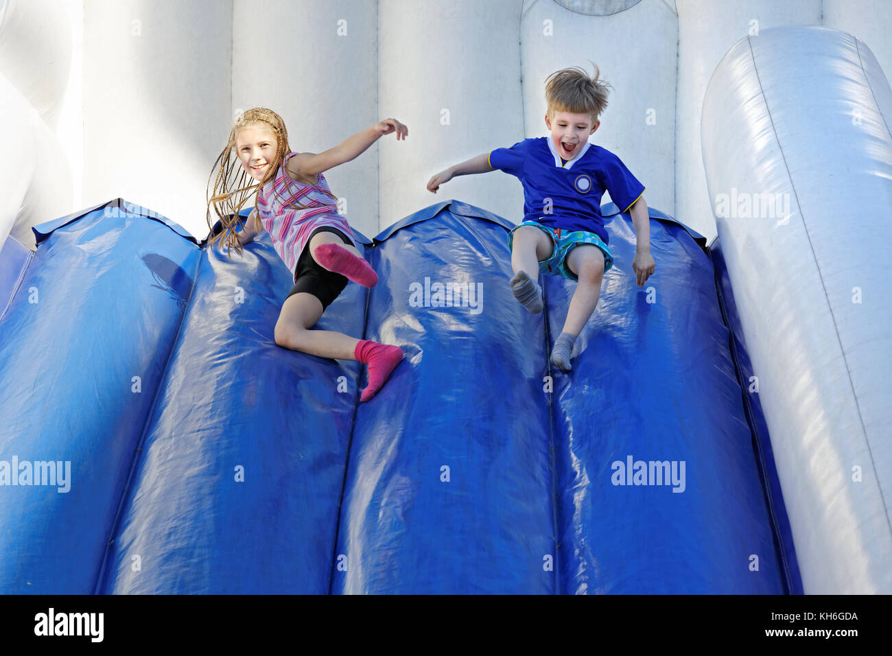 Children grimace and laugh as they roll down the smooth surface of the inflatable attraction Stock Photo