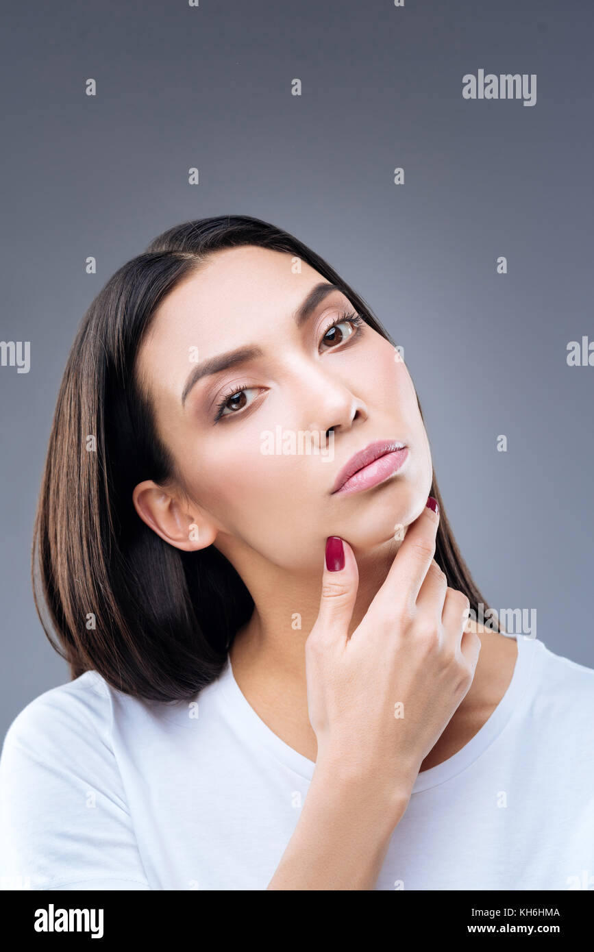 Young attentive woman touching her skin after using face cream Stock Photo