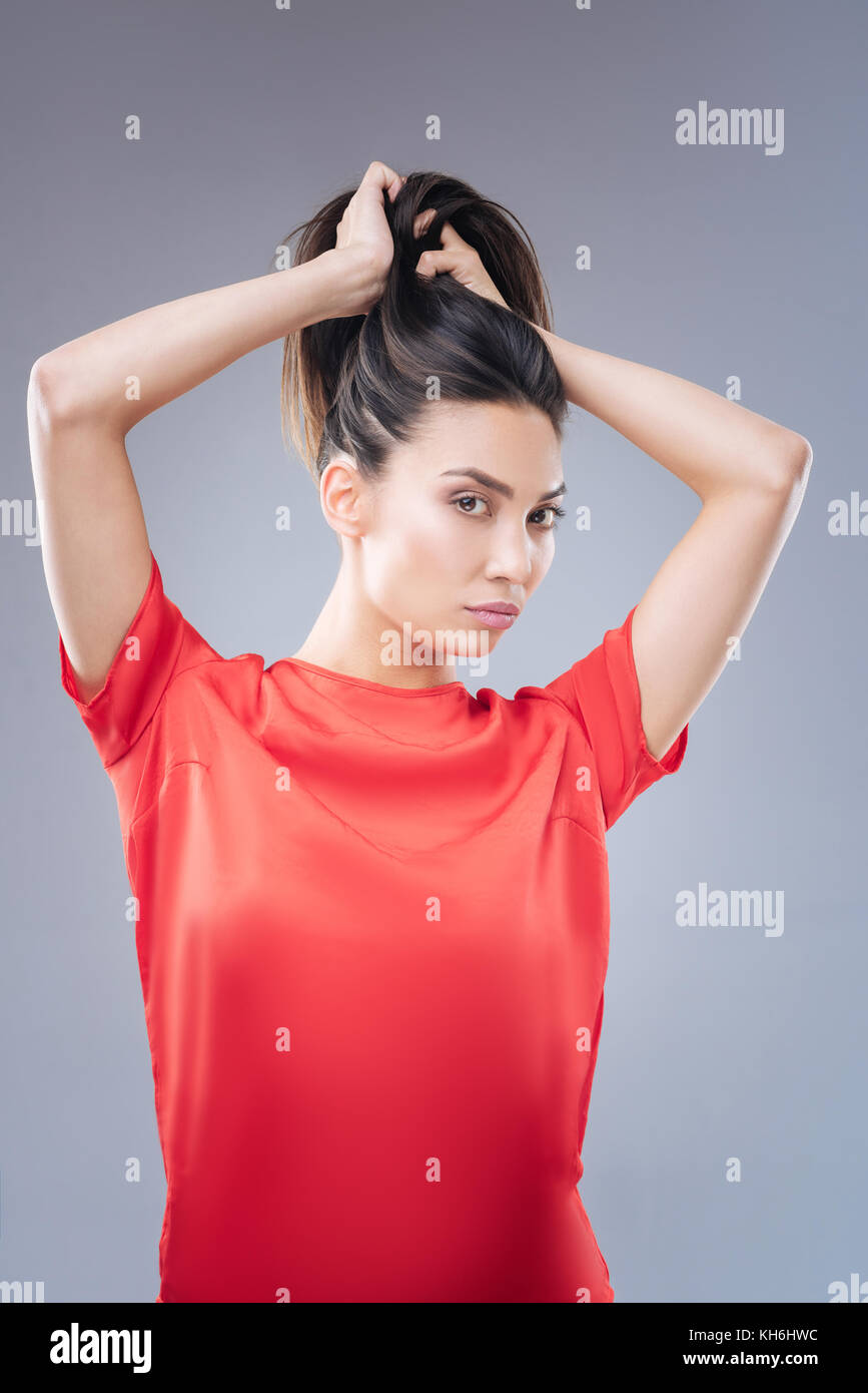 Beautiful calm woman making a nice ponytail while looking in the mirror Stock Photo