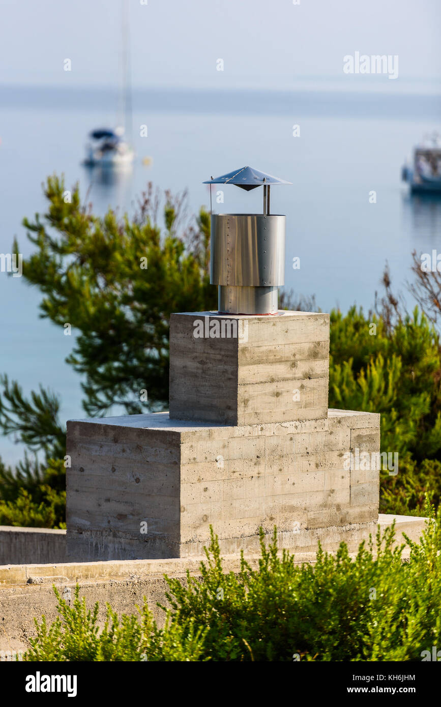 Modern fireplace grill chimney with sea and boats in backgrounds. Contemporary concrete barbecue chimney in Adriatic island. Stock Photo