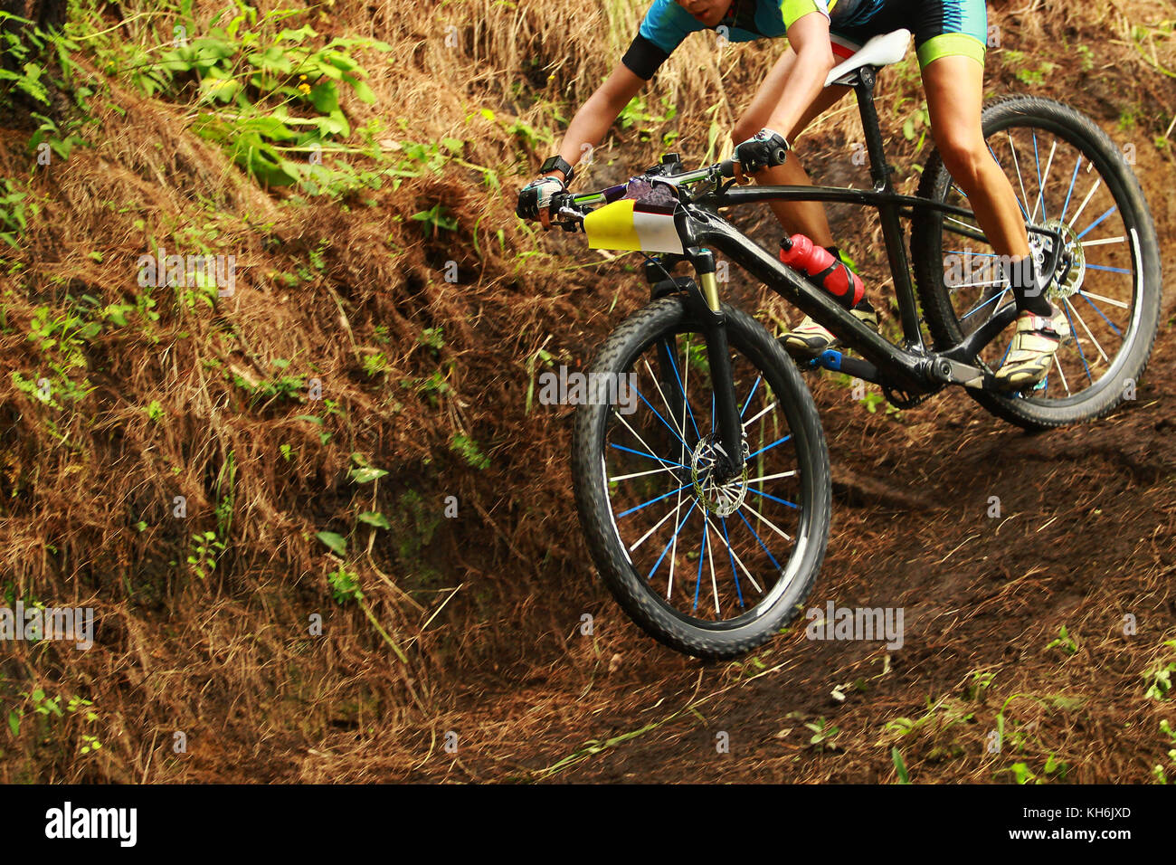 A young female cyclist going downhill on a muddy track during a cross country bike race in the forest Stock Photo
