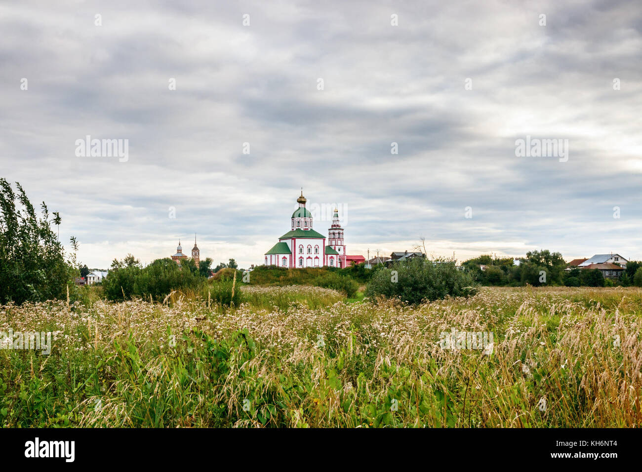 View of Suzdal with the St Elijah Church and a field with green grasses and white flowers under a cloudy sky, Suzdalsky District, Golden Ring, Russia. Stock Photo
