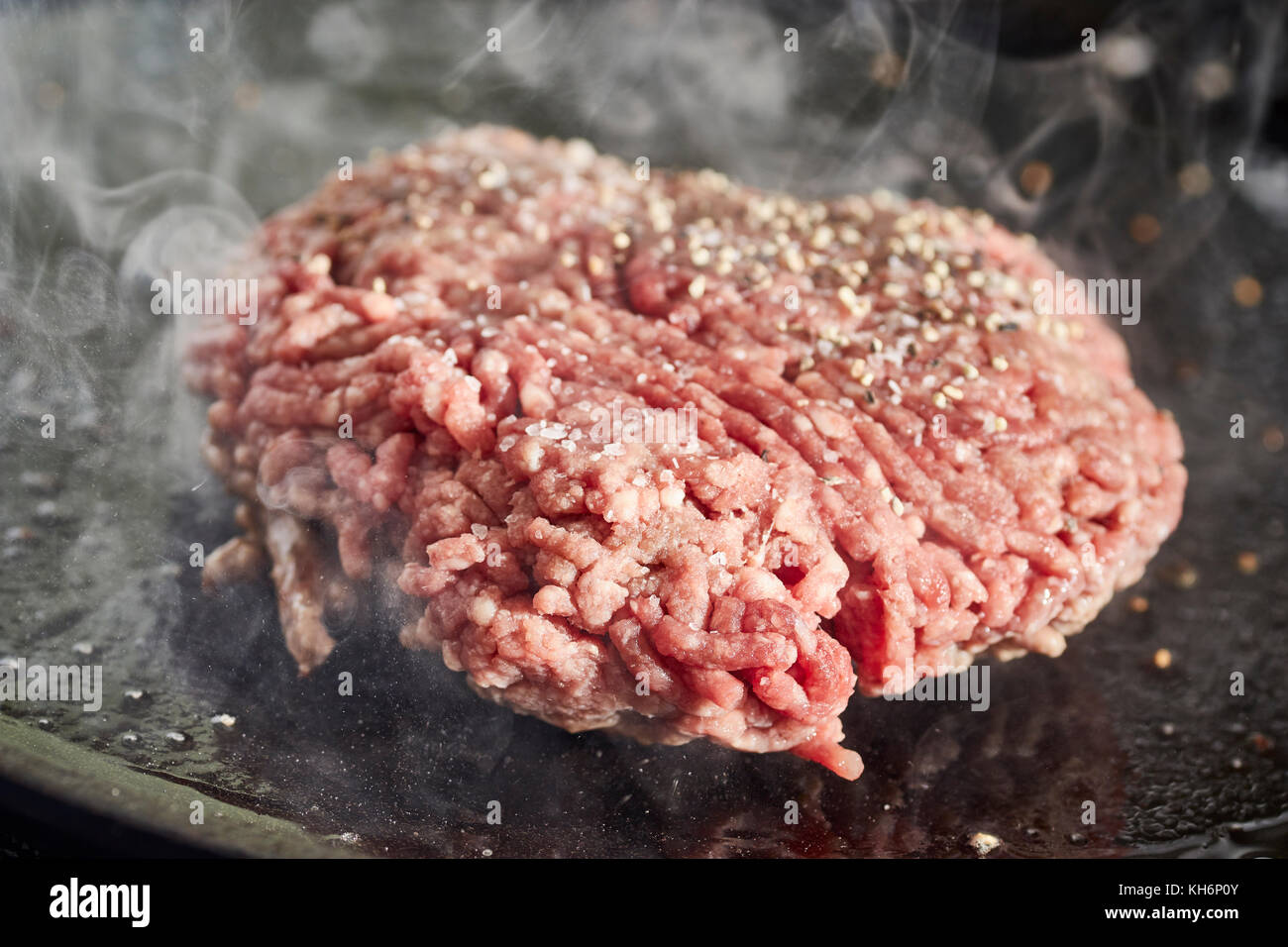 A hamburger patty frying on a cast iron grill Stock Photo Alamy