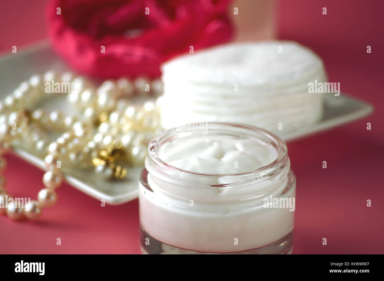 A jar of luxury beauty face cream and serum bottle with pearls on pink
