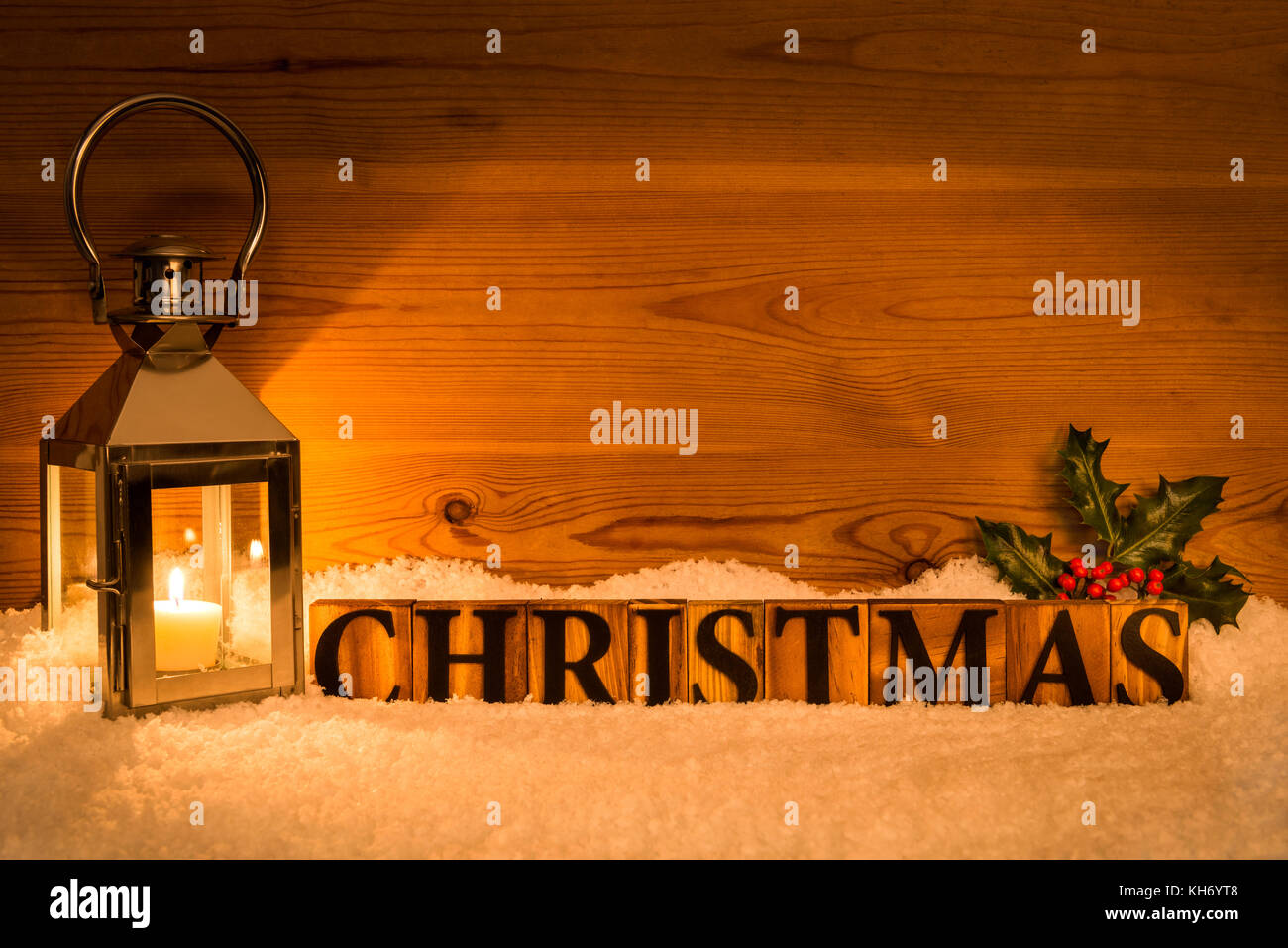 The word Christmas next to lantern with candle inside on a snow and wod background with holly Stock Photo