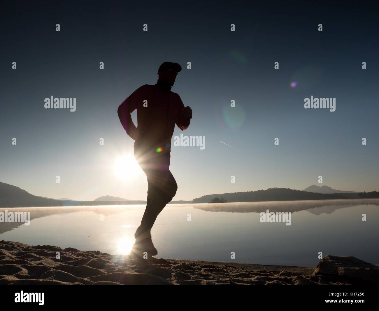Tall fit man running fast by the sea on the beach. Powerful runner training outdoor in summer