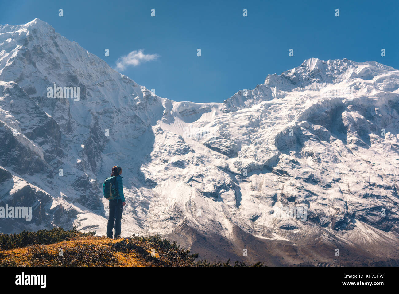 Standing young woman on the hill and looking on amazing Himalayan mountains. Landscape with traveler, high rocks with snowy peaks, blue sky in autumn  Stock Photo
