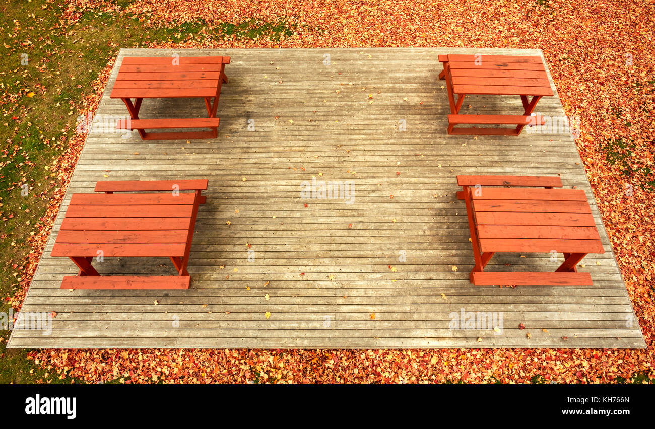 Pole aerial High Dynamic Range (HDR) image of four picnic tables on a wooden platform surrounded by autumn leaves and grass. Stock Photo