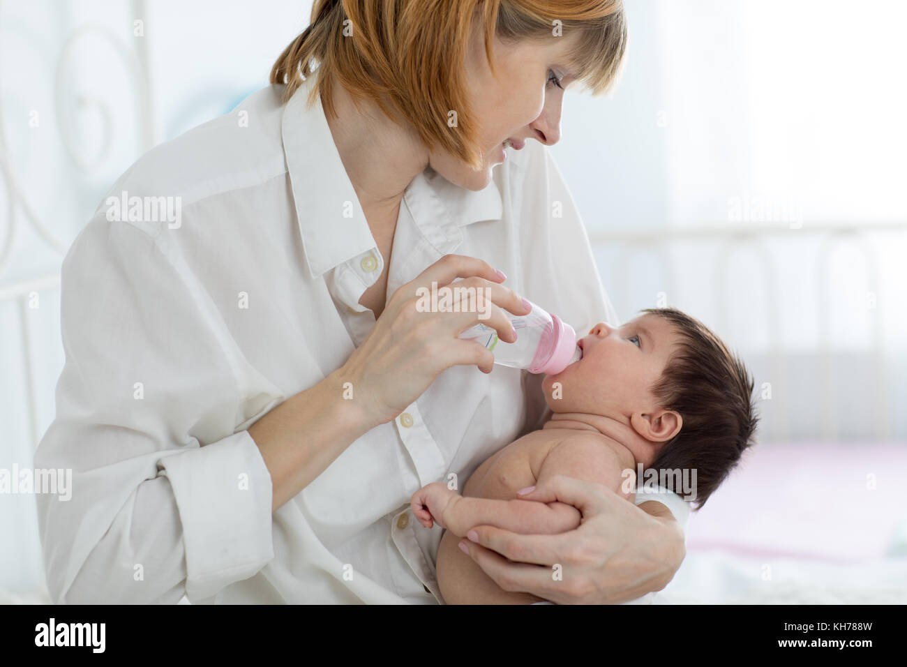 Mom holding and giving water to baby infant from bottle Stock Photo