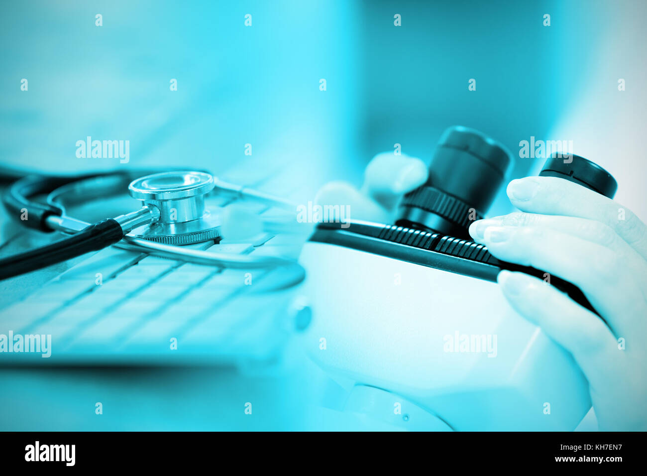 Close-up of keyboard with stethoscope against close up of a female scientist looking through a microscope Stock Photo