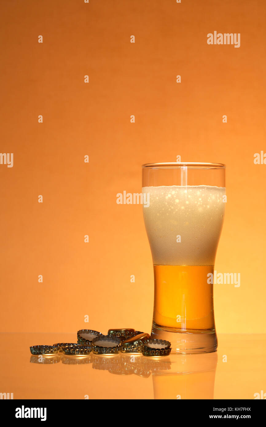 Bottle caps lying near glass of light beer with foam Stock Photo Alamy