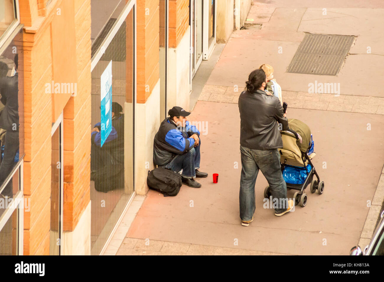 A beggar outside Monop' convenience store, Place Victor Hugo, Toulouse, Occitanie, France Stock Photo