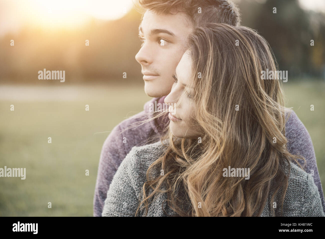 Young loving couple outdoors sitting on grass, hugging and looking away, future and relationships concept Stock Photo