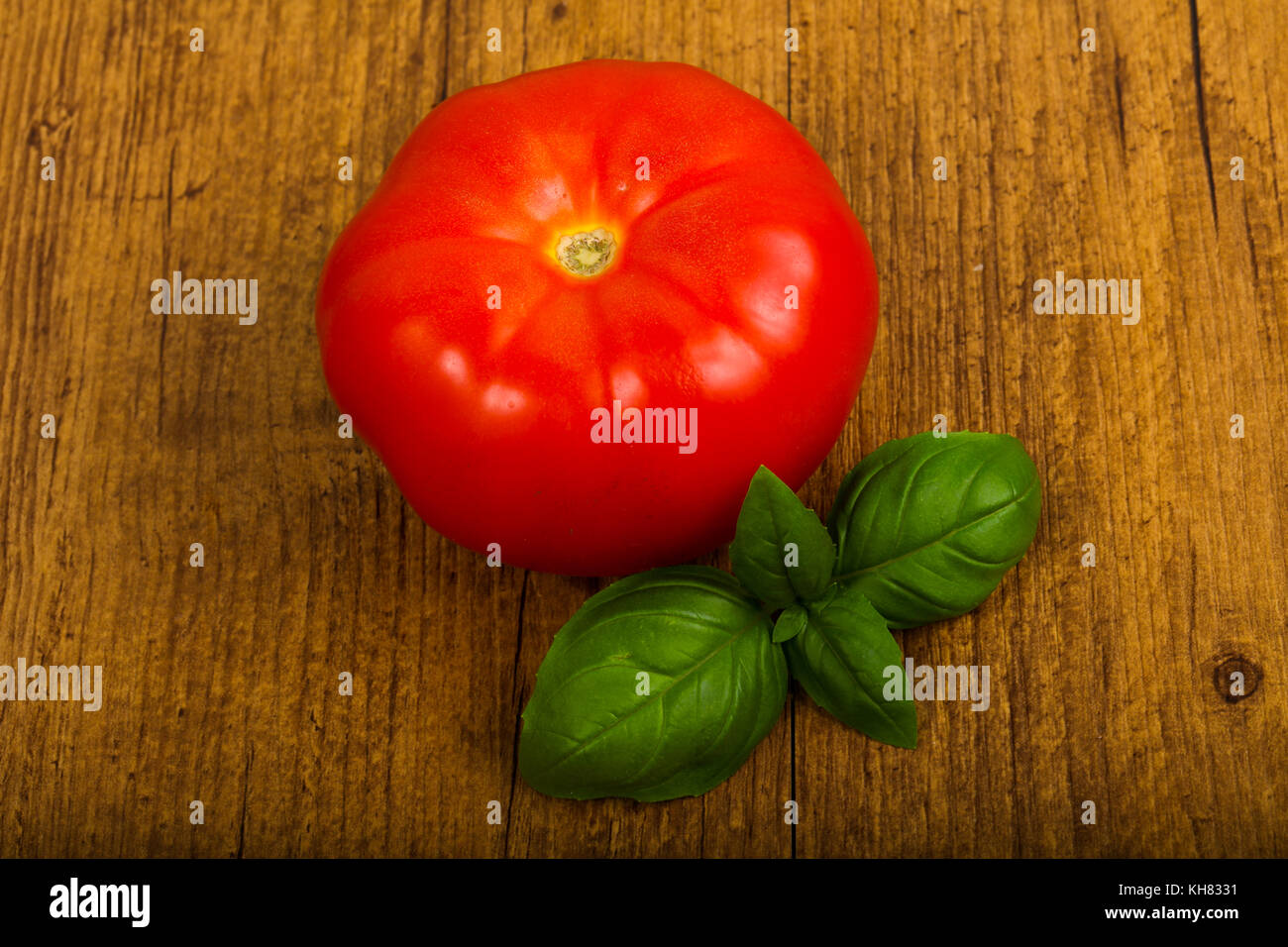 Tomato with basil leaves over wooden background Stock Photo - Alamy