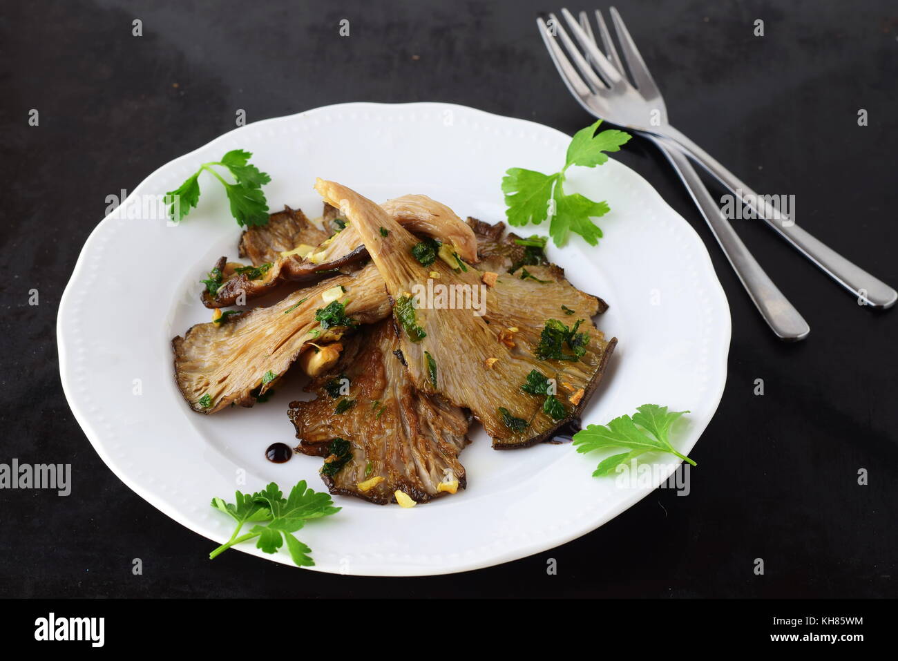 Fried Oyster mushrooms with garlic, parsley and balsamic glaze in a white plate on a black abstract background. Healthy concept. Stock Photo