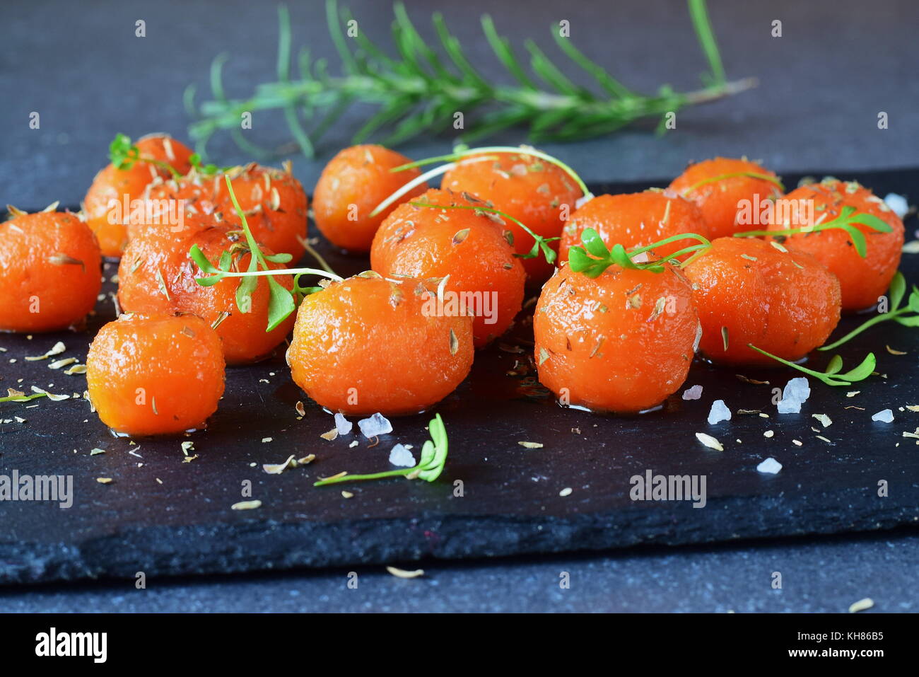 Honey glazed baby carrots with sea salt and thyme on a grey abstract background. Healthy eating concept. Fasting food. Healthy meal Stock Photo