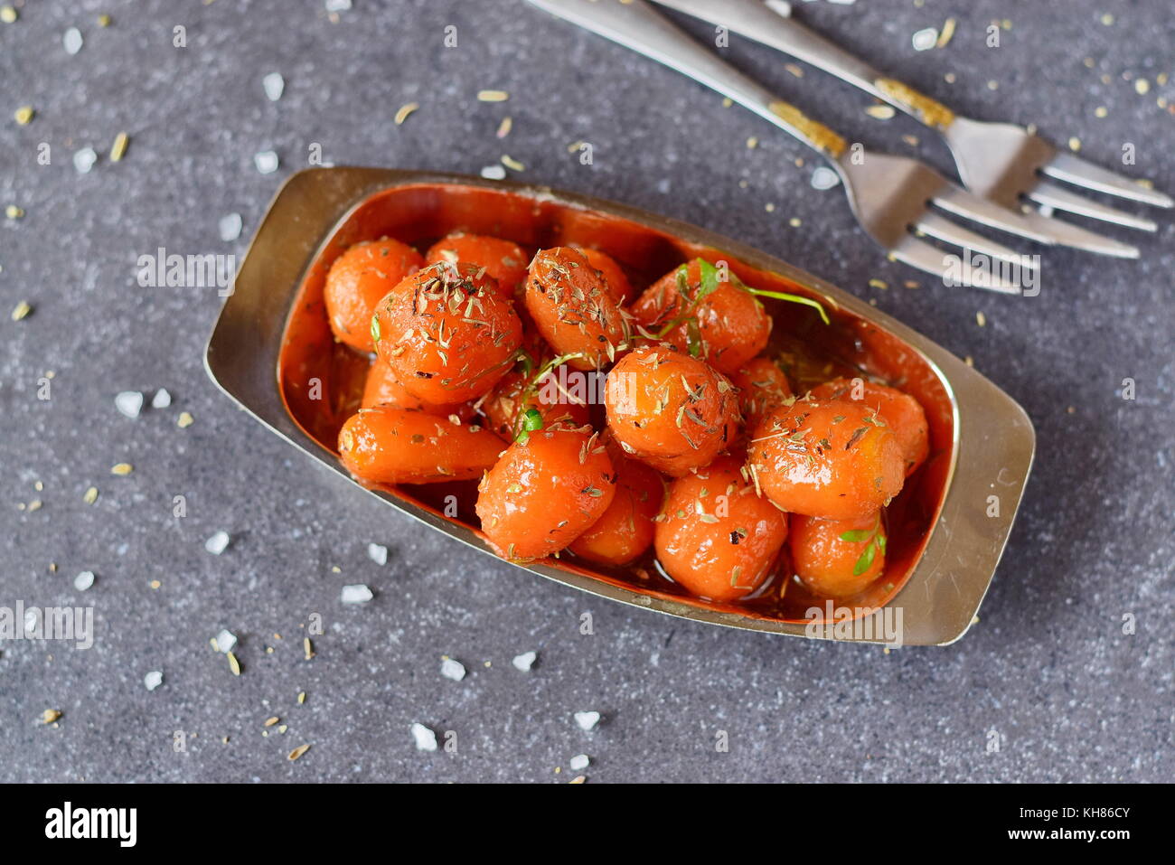 Honey glazed baby carrots with sea salt and thyme in a metal bowl on a grey abstract background. Healthy eating concept. Fasting food. Healthy meal Stock Photo