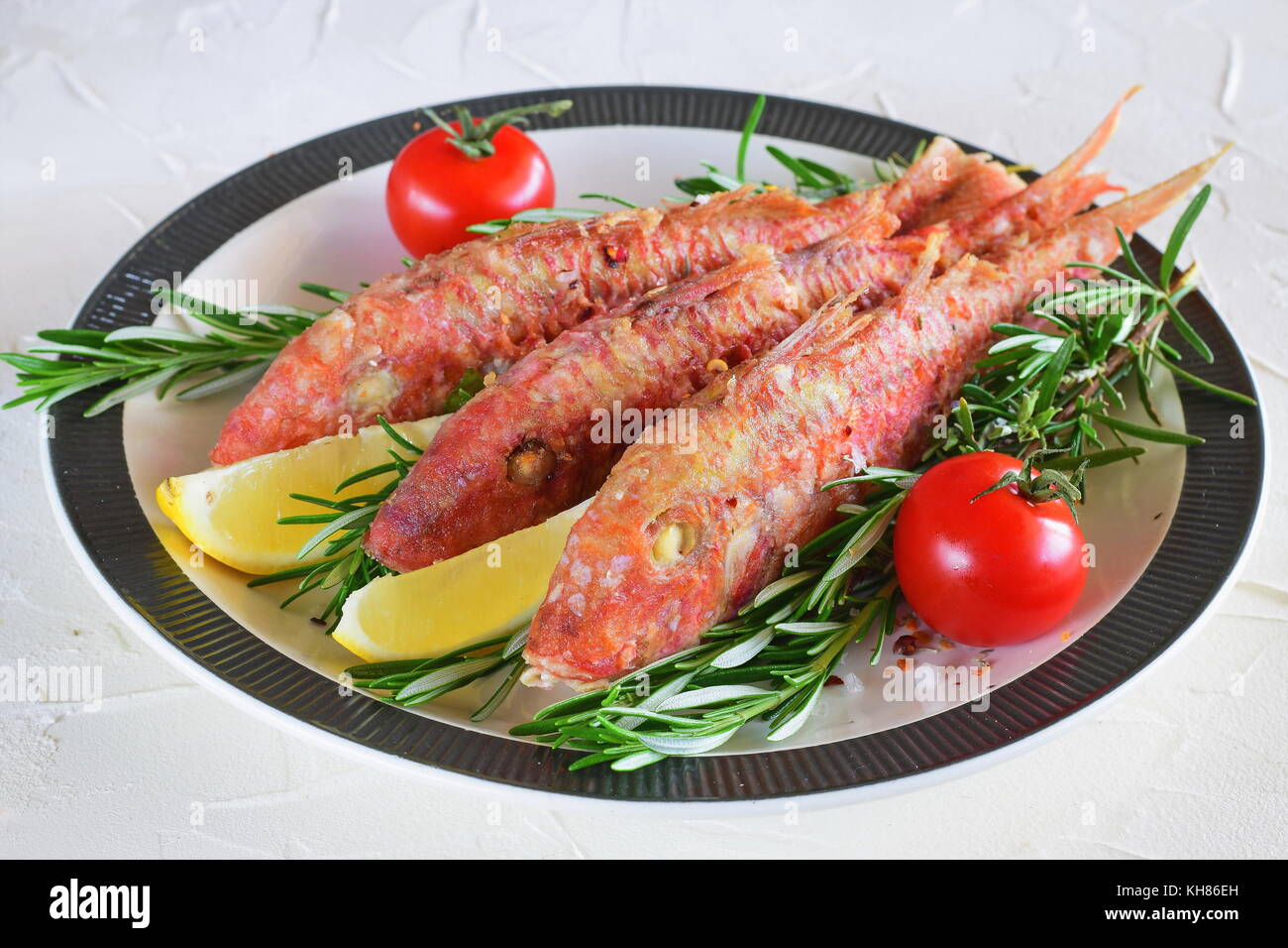 Grilled red mullet in a plate with herbs, tomato and lemon. Healthy food. Mediterranean lifestyle. Stock Photo