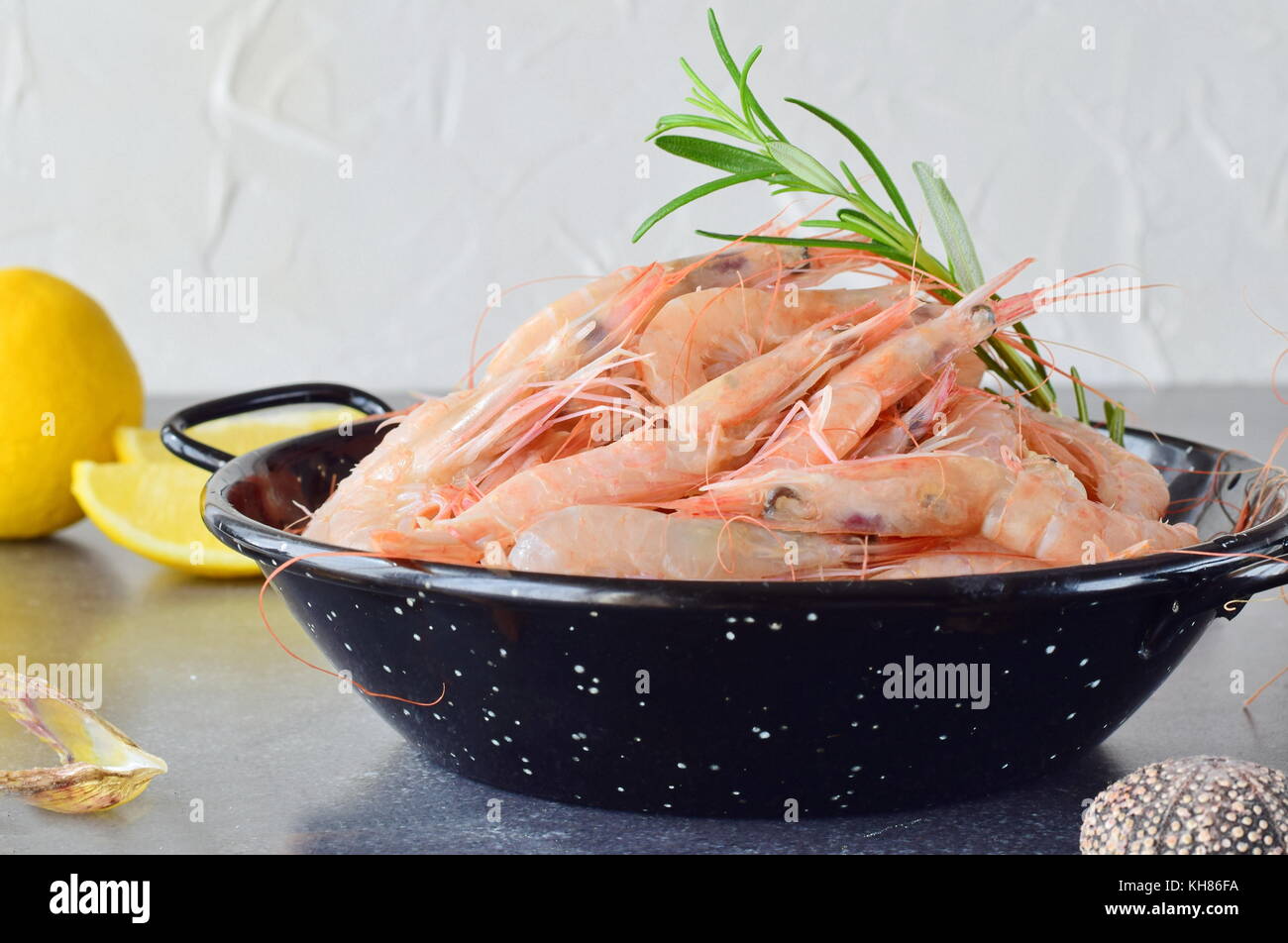 Raw fresh shrimps in a black metal bowl with rosemary on a grey background. Mediterranean lifestyle. Healthy food Stock Photo