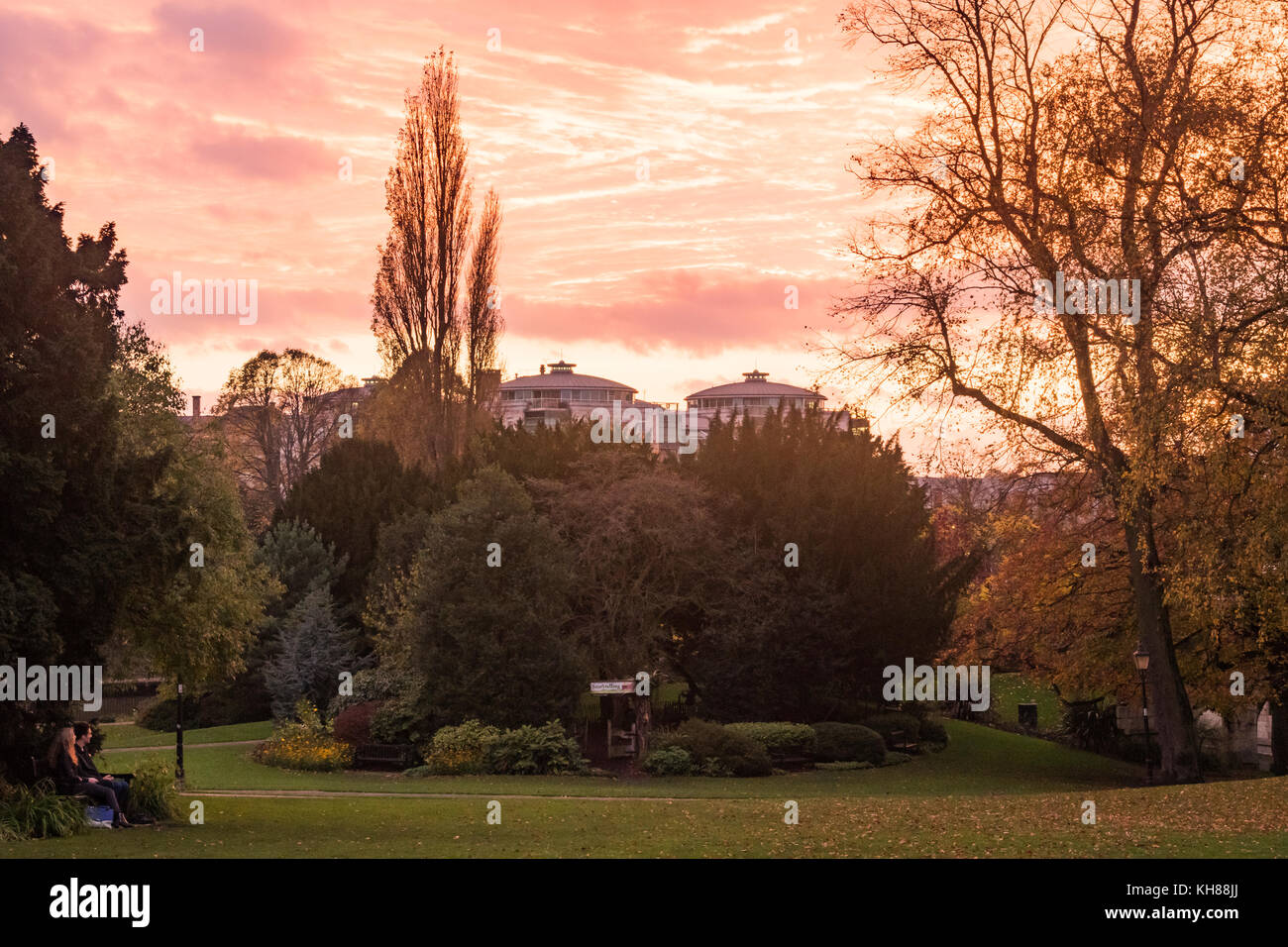 Beautiful, dramatic, autumn, evening sunset with red sky over peaceful Museum Gardens, is admired by couple sitting on bench -  York, England, UK. Stock Photo