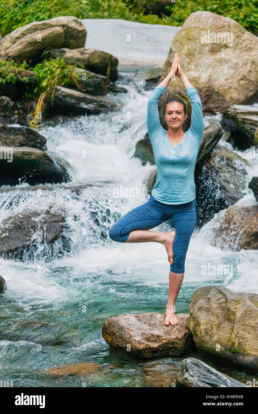 Woman in yoga asana Vrikshasana tree pose at waterfall outdoors Stock Photo