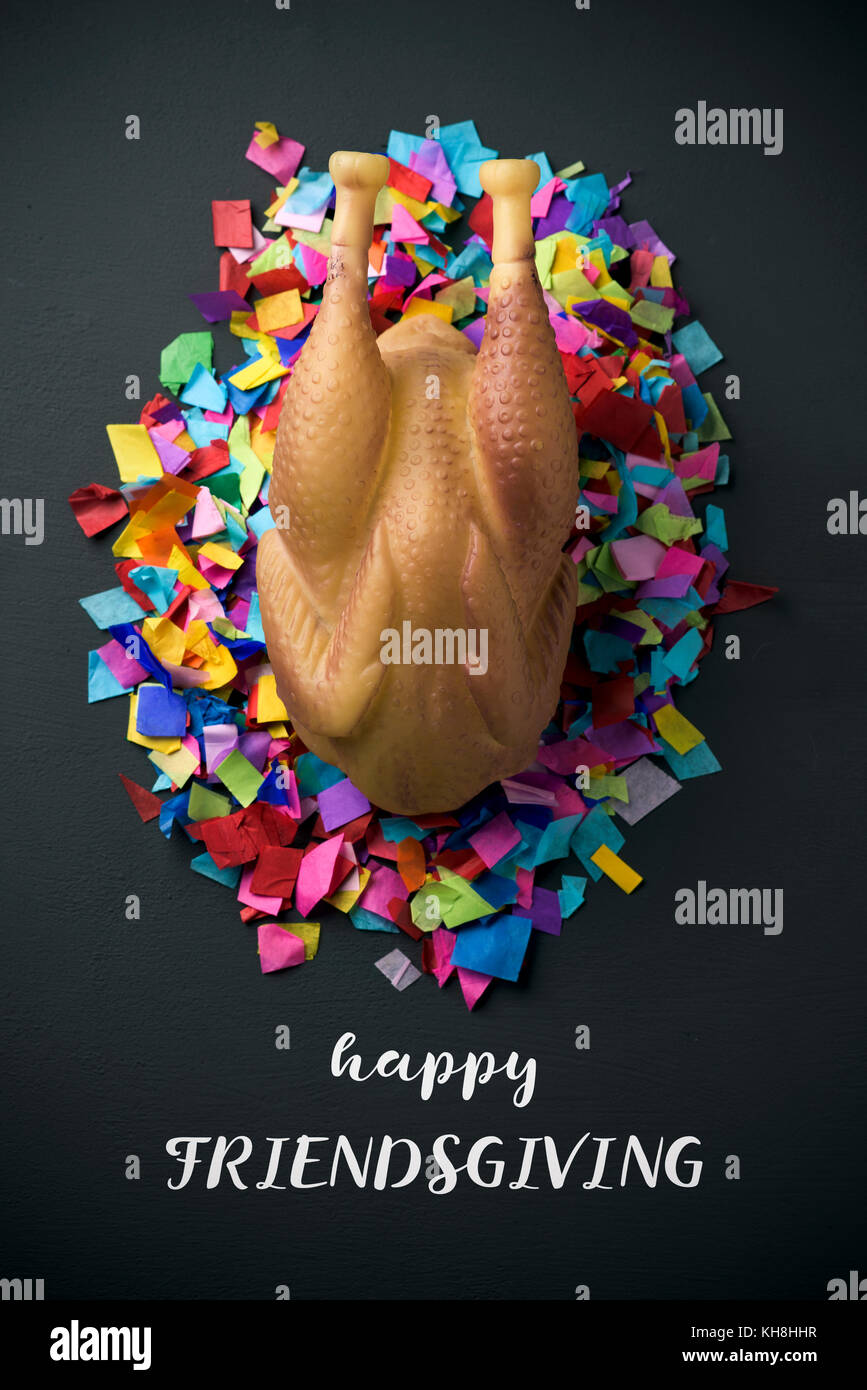 high-angle shot of a rubber roast turkey on a pile of confetti, placed on a rustic surface, and the text happy friendsgiving Stock Photo