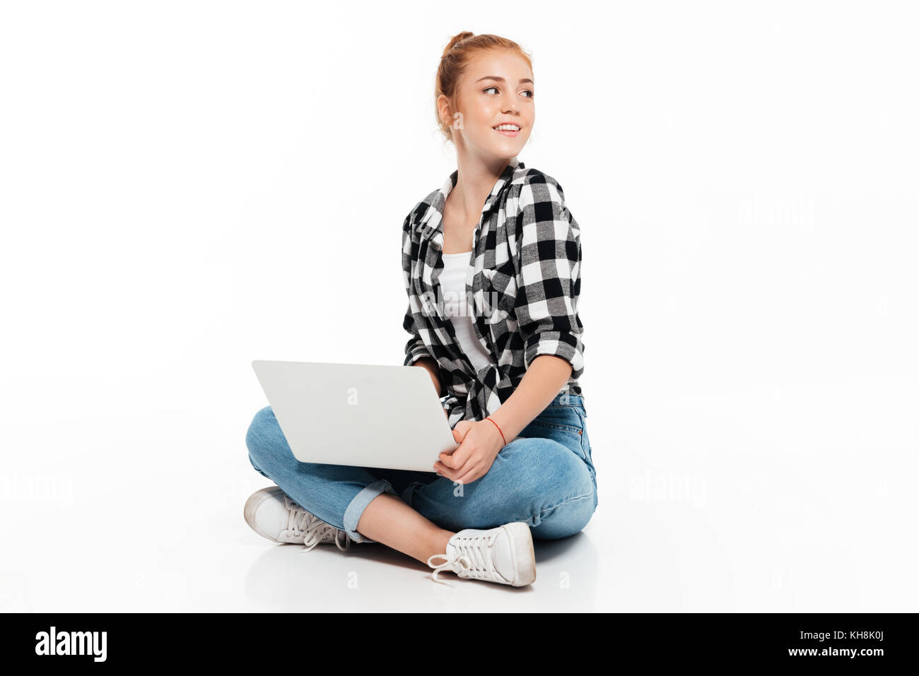 Happy ginger woman in shirt and jeans sitting on the floor with laptop ...