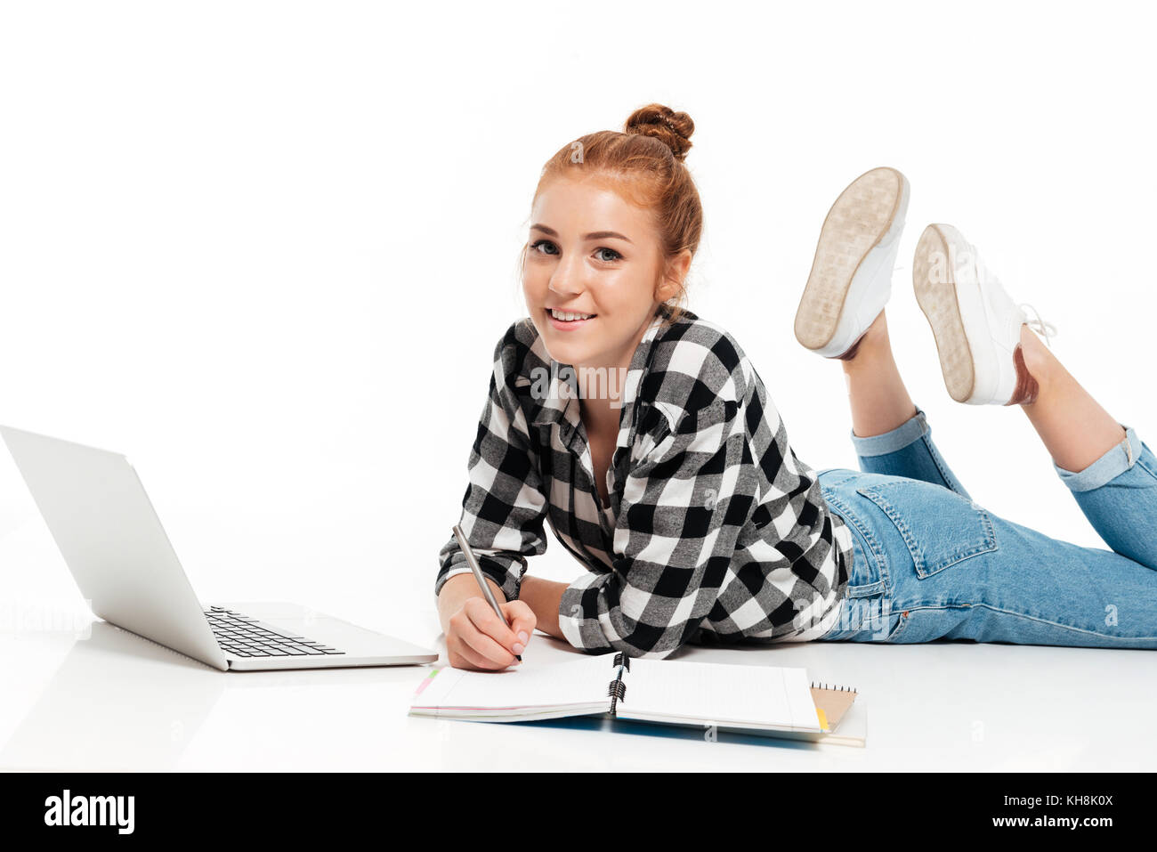 Happy ginger woman in shirt and jeans lying on the floor with laptop ...