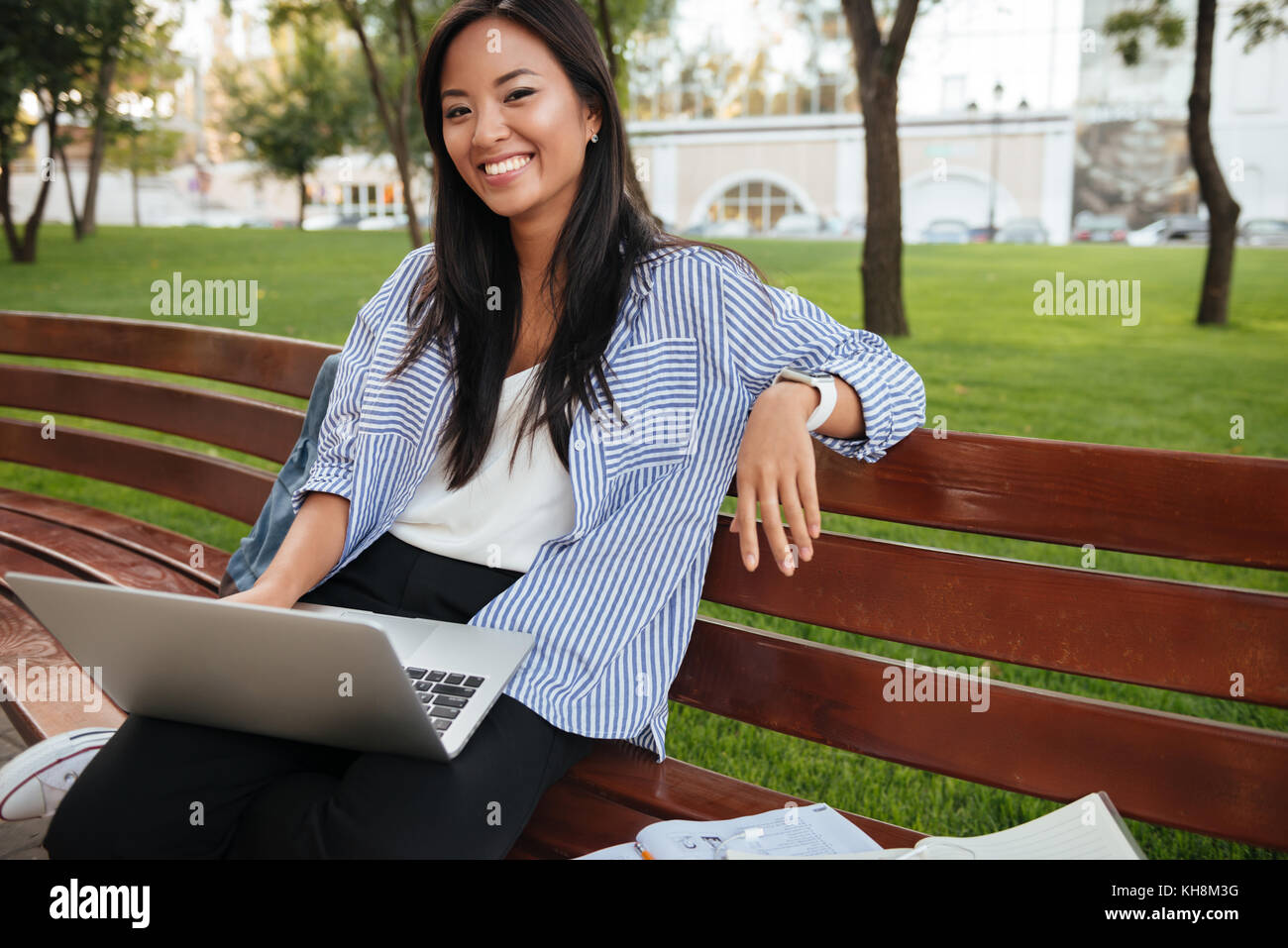 Portrait of laughing pretty asian woman, relaxing in park with laptop, looking at camera Stock Photo