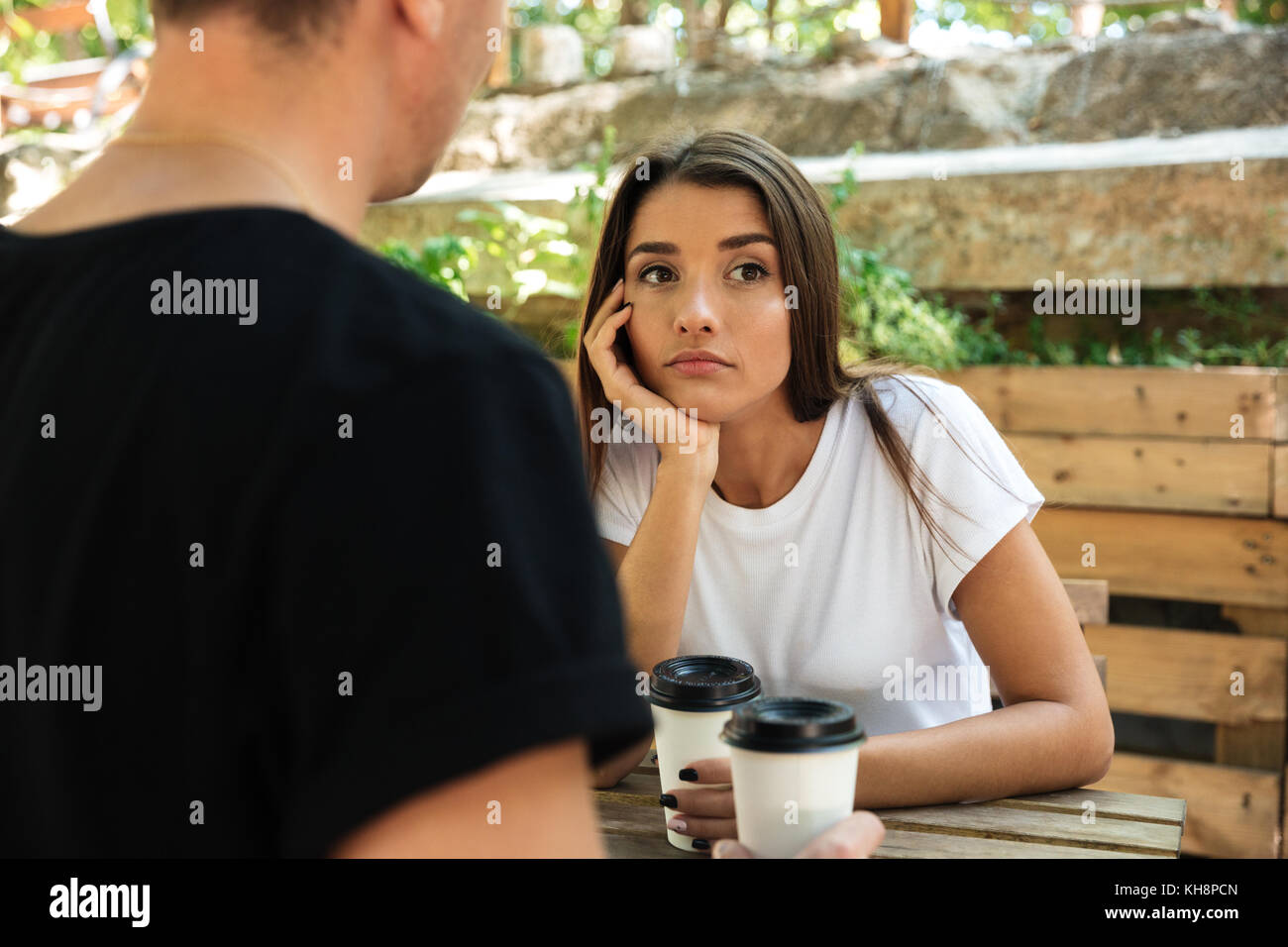 Young bored girl sitting and drinking coffee with her boyfriend at a cafe outdoors Stock Photo